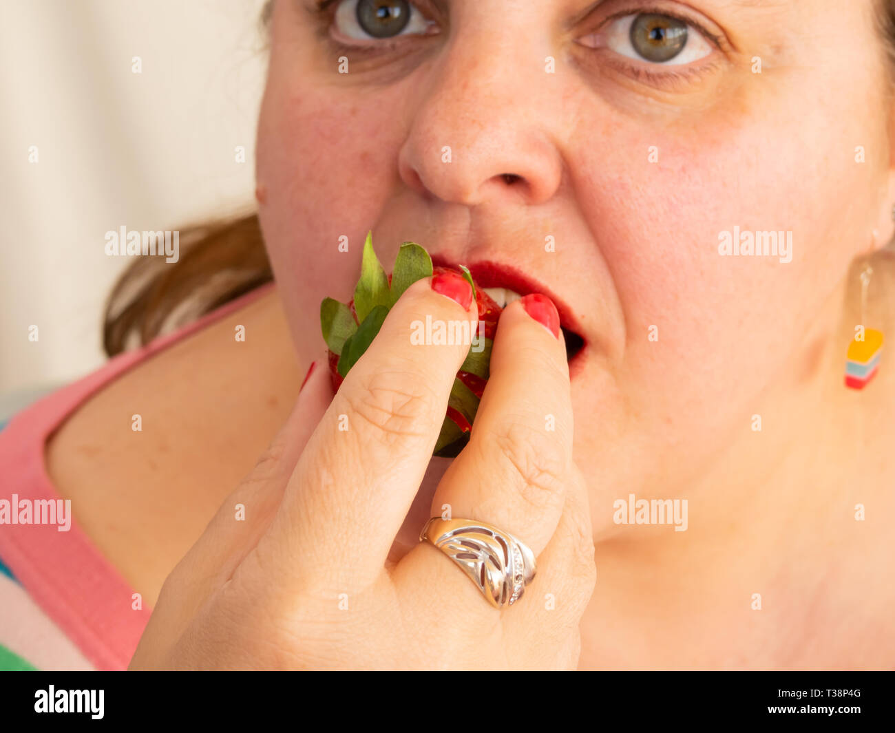 Eine erwachsene Frau mit roten Nägeln und Lippen essen eine Erdbeere Stockfoto