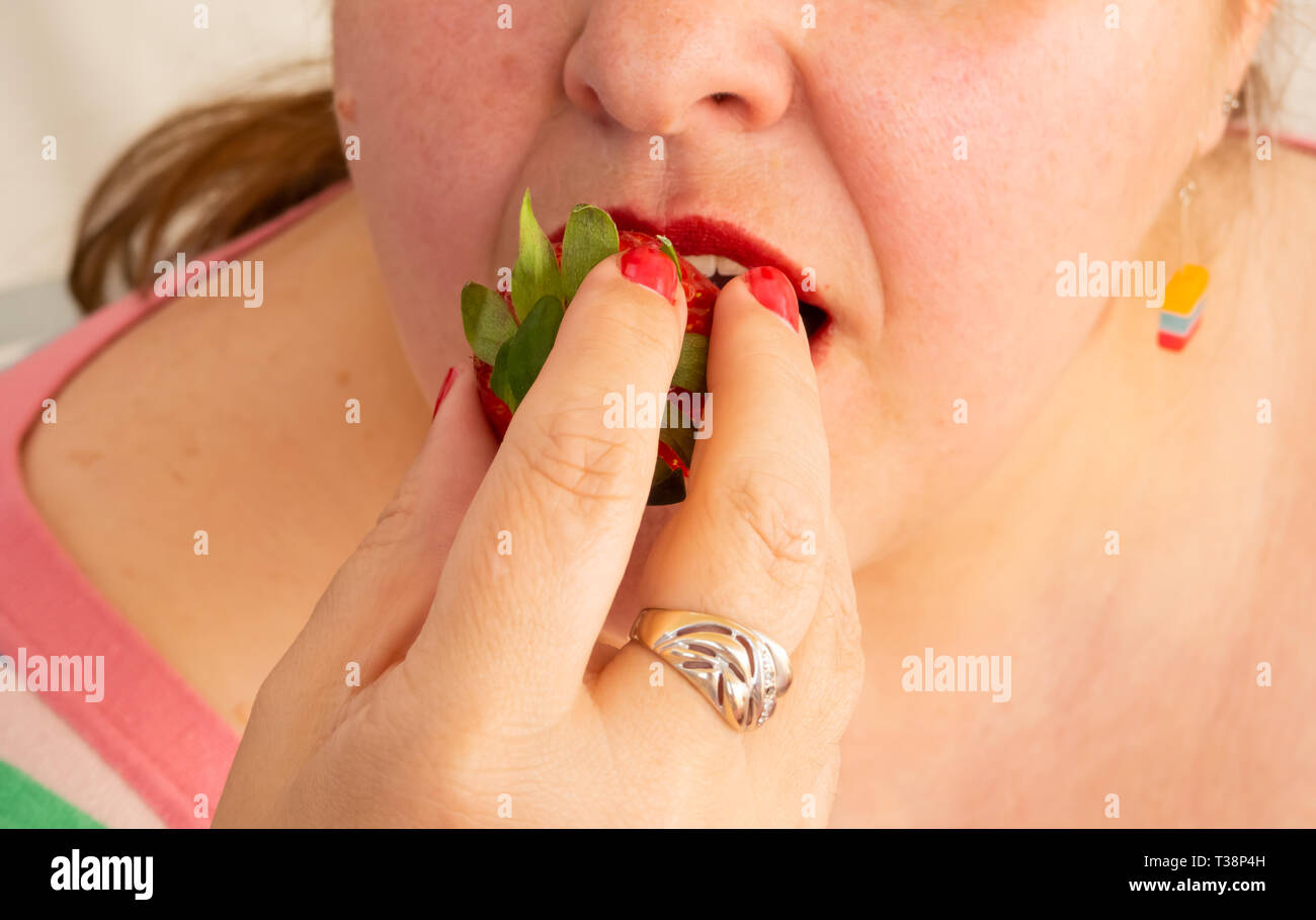 Eine erwachsene Frau mit roten Nägeln und Lippen essen eine Erdbeere Stockfoto