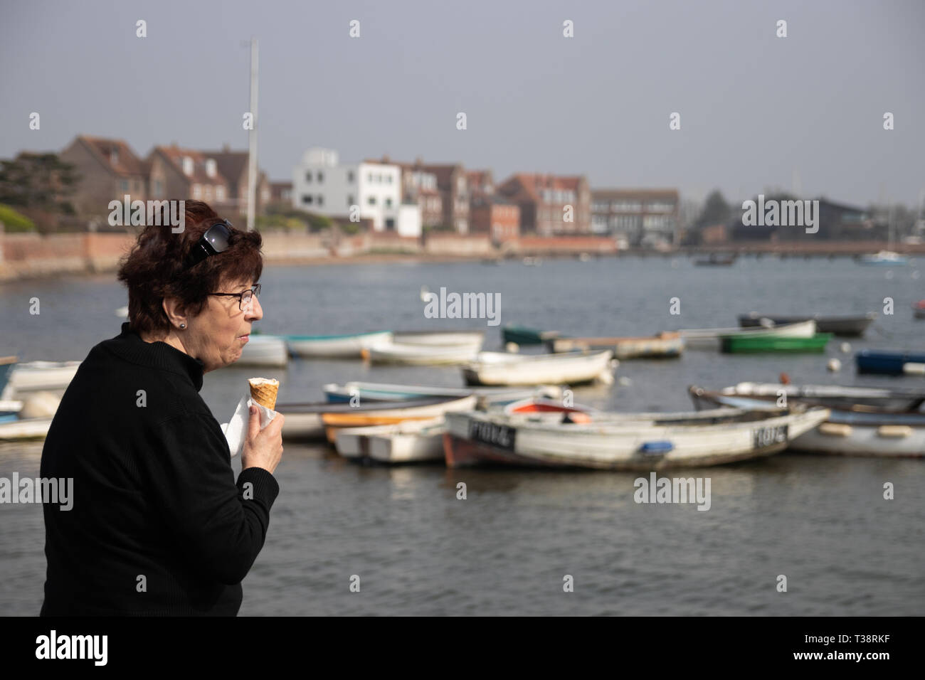 Dame mittleren Alters essen Eis am Meer mit Booten im Hintergrund Stockfoto