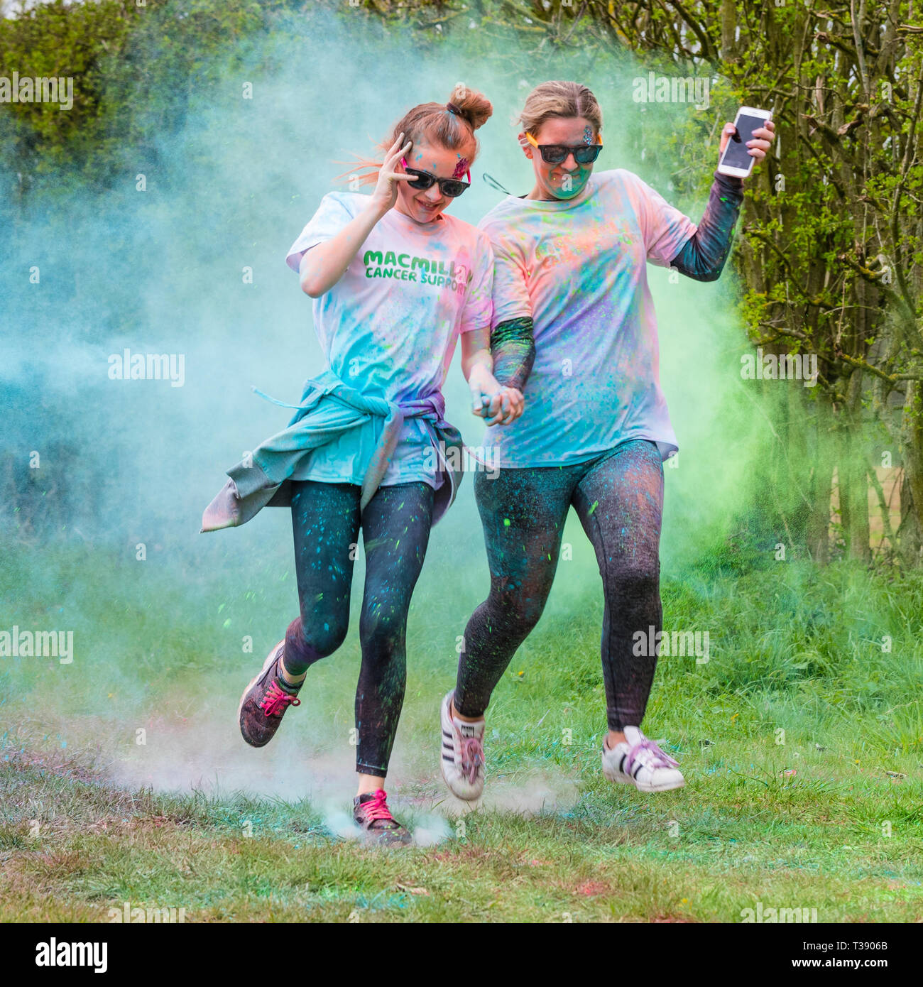 Zwei Frauen schienen, einer Holding ein smart phone, in Farbe auf Macmillan Cancer Charity 5K Farbe Fun Run wird abgedeckt. Stockfoto