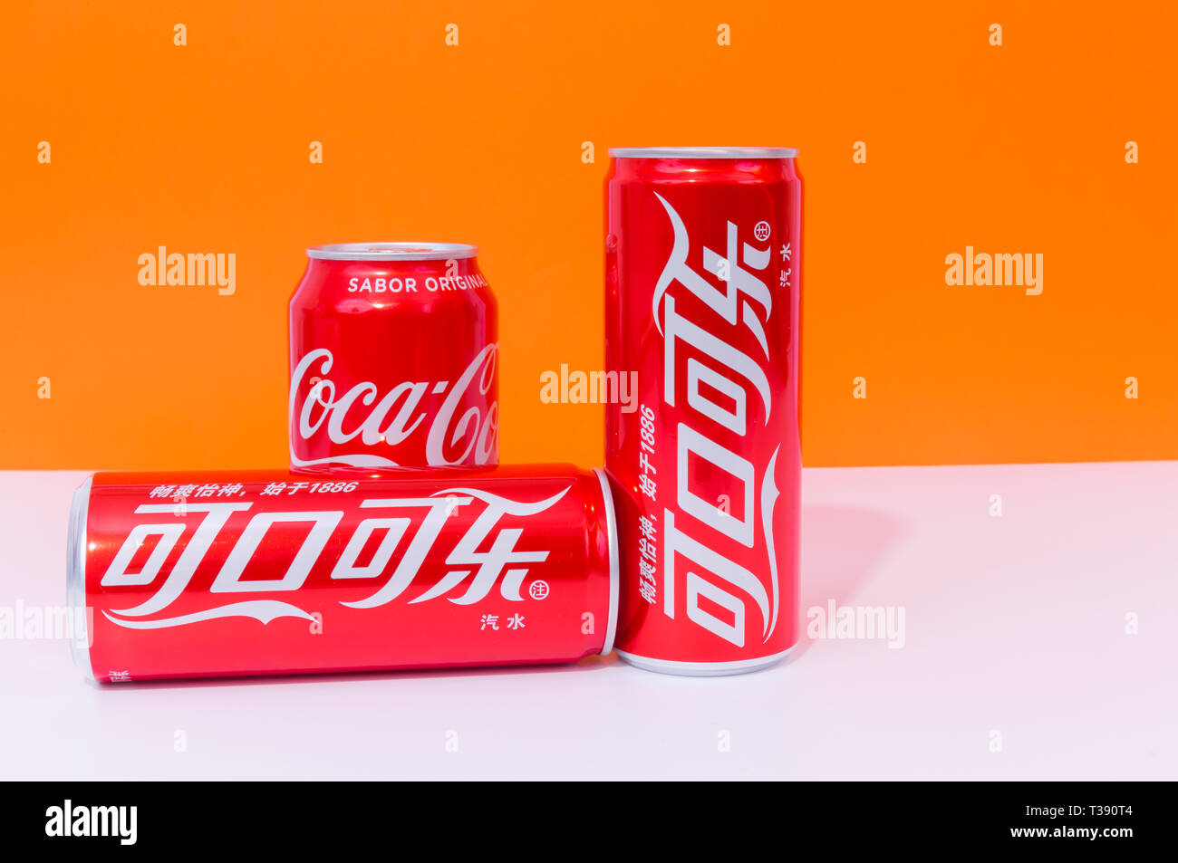 Peniscola, Castellon, Spanien - 07 April 2019: drei Dosen Cola, zwei in Chinesisch geschrieben, Getränke auf einem orange Farbe Hintergrund isoliert. Die nicht-Alcoh Stockfoto
