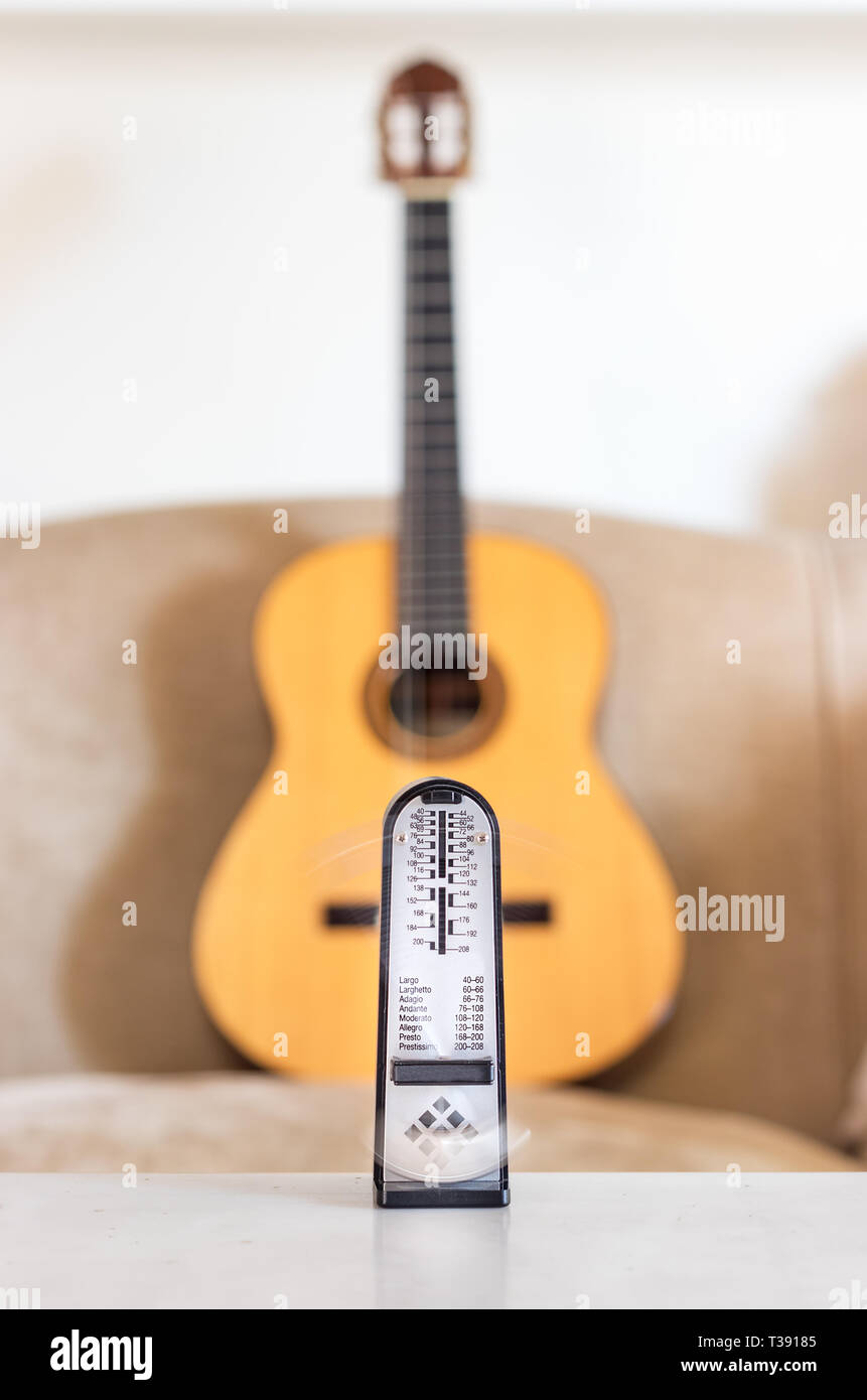 Mechanische Metronome in Bewegung, über eine hölzerne klassische Gitarre Hintergrund. Stockfoto