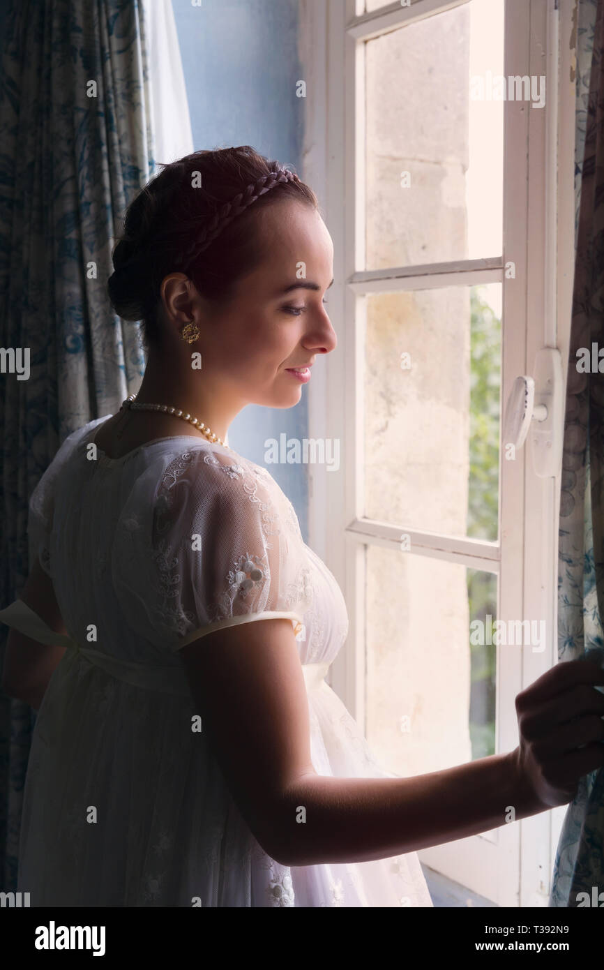 Junge Frau in authentischen Regency Kleid in der Nähe von einem Fenster eines klassischen Interieur Stockfoto