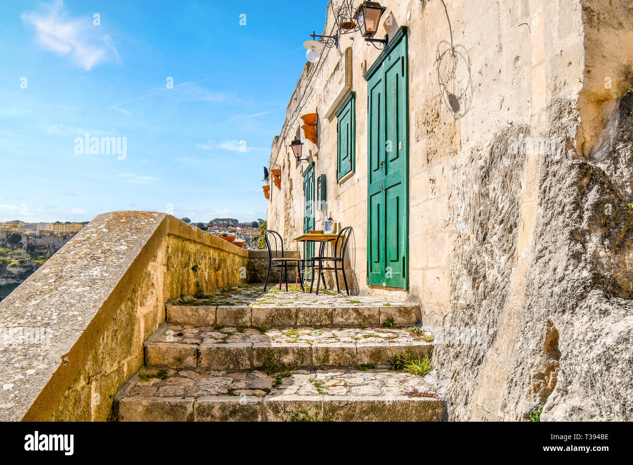Zwei Stühle und einen Tisch mit einer Flasche Wein sitzen auf einer kleinen Terrasse draußen eine grüne Tür und Verschluss in der antiken Stadt Matera, Italien. Stockfoto