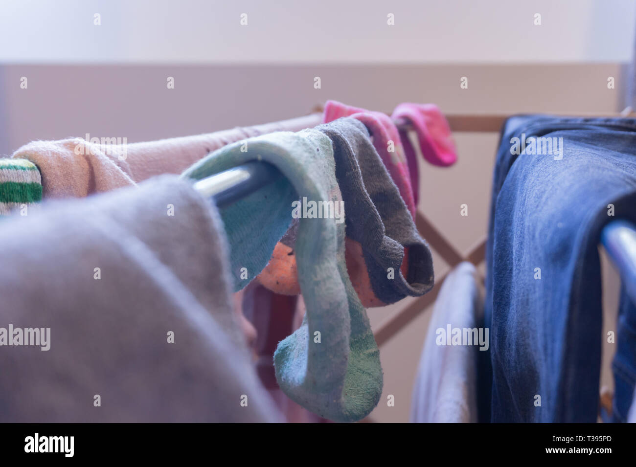 Fokus auf Söckchen trocknen auf einem Wäscheständer mit der Kleidung der anderen Frau, einschließlich Blue Jeans. Nicht zusammenpassende Socken und ein paar abgestimmte Socken. Stockfoto