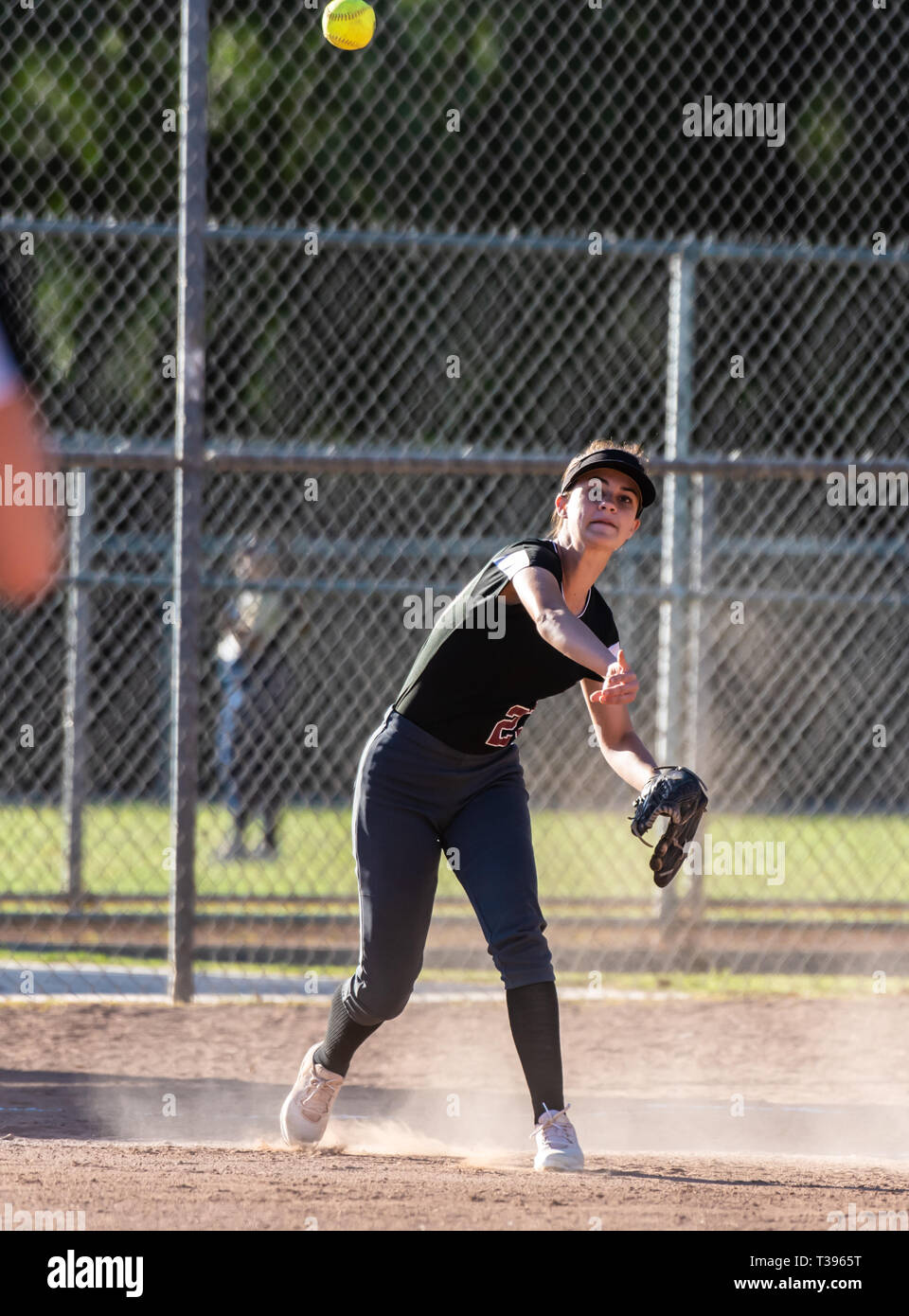 Weibliche Jugend Softball Spieler in der schwarzen Uniform werfen Kugel über infield Für die in eine Wolke von Staub. Stockfoto