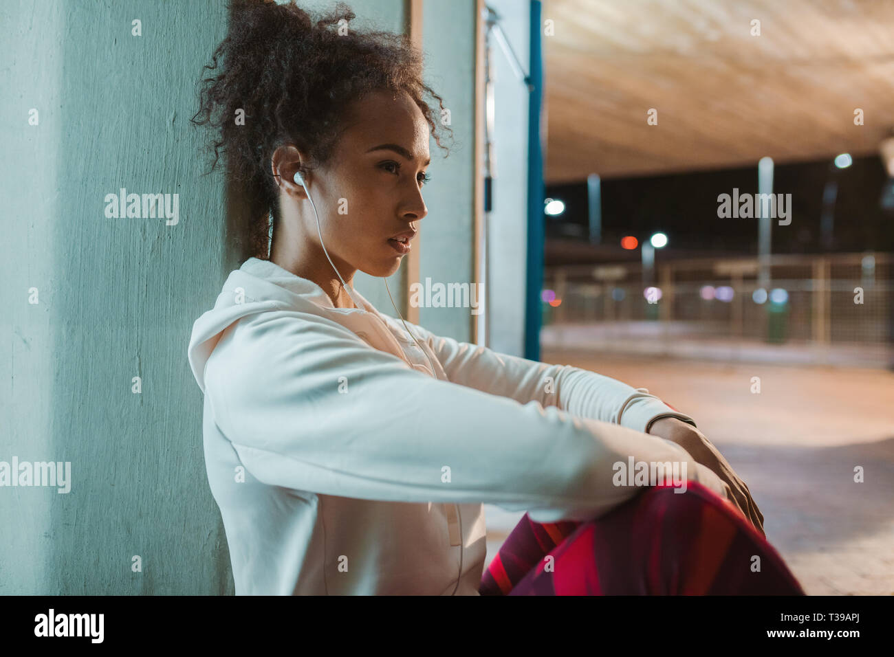 Seitenansicht der jungen Frau, die unter einer Brücke sitzt und der Rest nach dem Ausführen der Übung. Urban runner Ausruhen nach der Ausbildung in der Nacht. Stockfoto