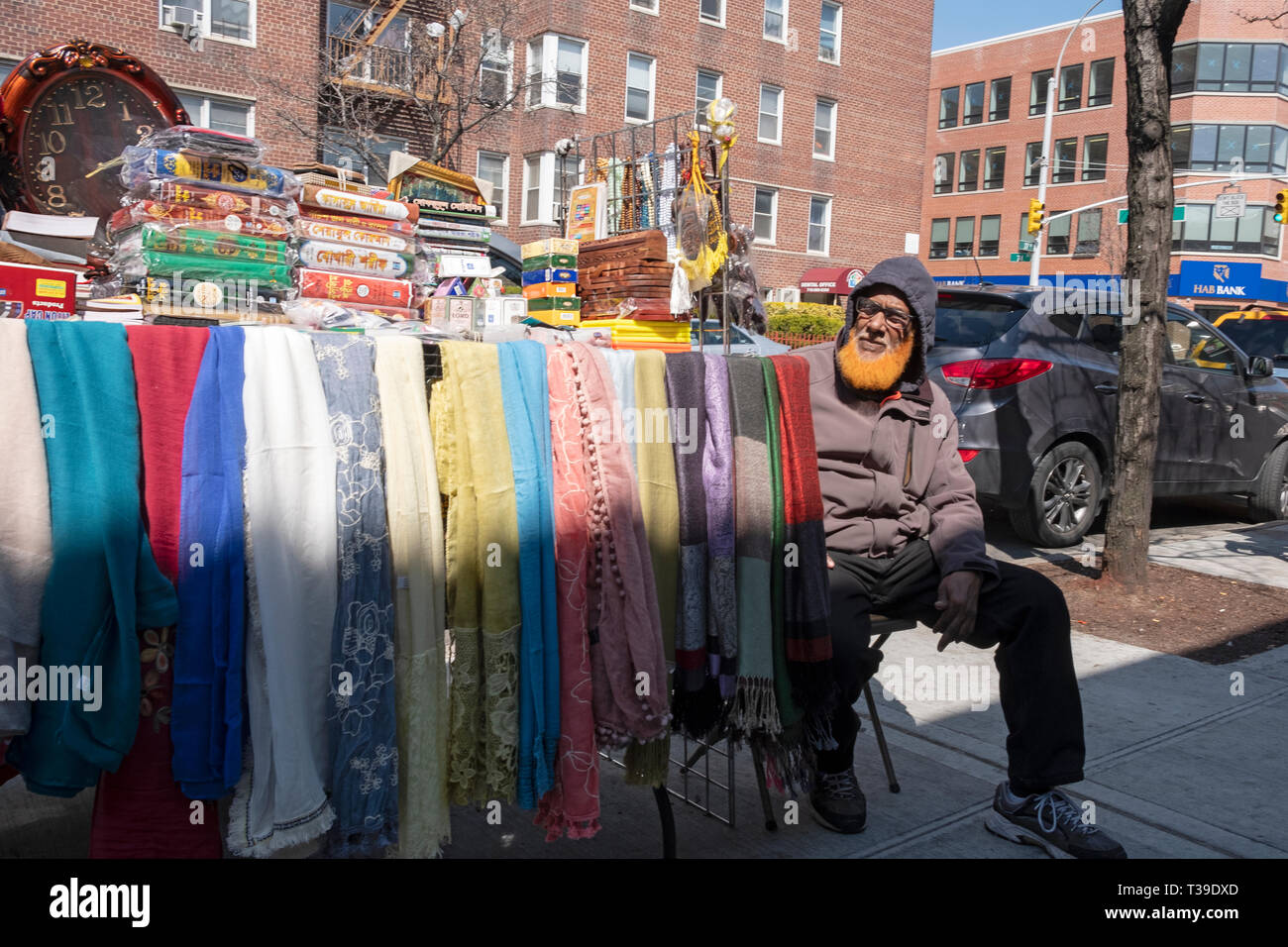 Ein Muslimischer Mann mit seinem Bart gefärbt Orange, Verkauf von Textilien, Bücher & religiöse Elemente auf die 37th Avenue in Jackson Heights, Queens, New York City. Stockfoto