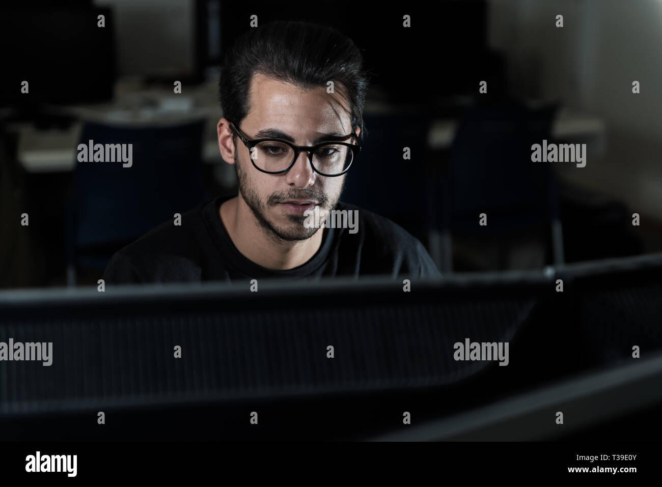 Blick über einen Bildschirm auf dem Gesicht eines jungen Informatik Schüler arbeiten mit dem Computer. Stockfoto