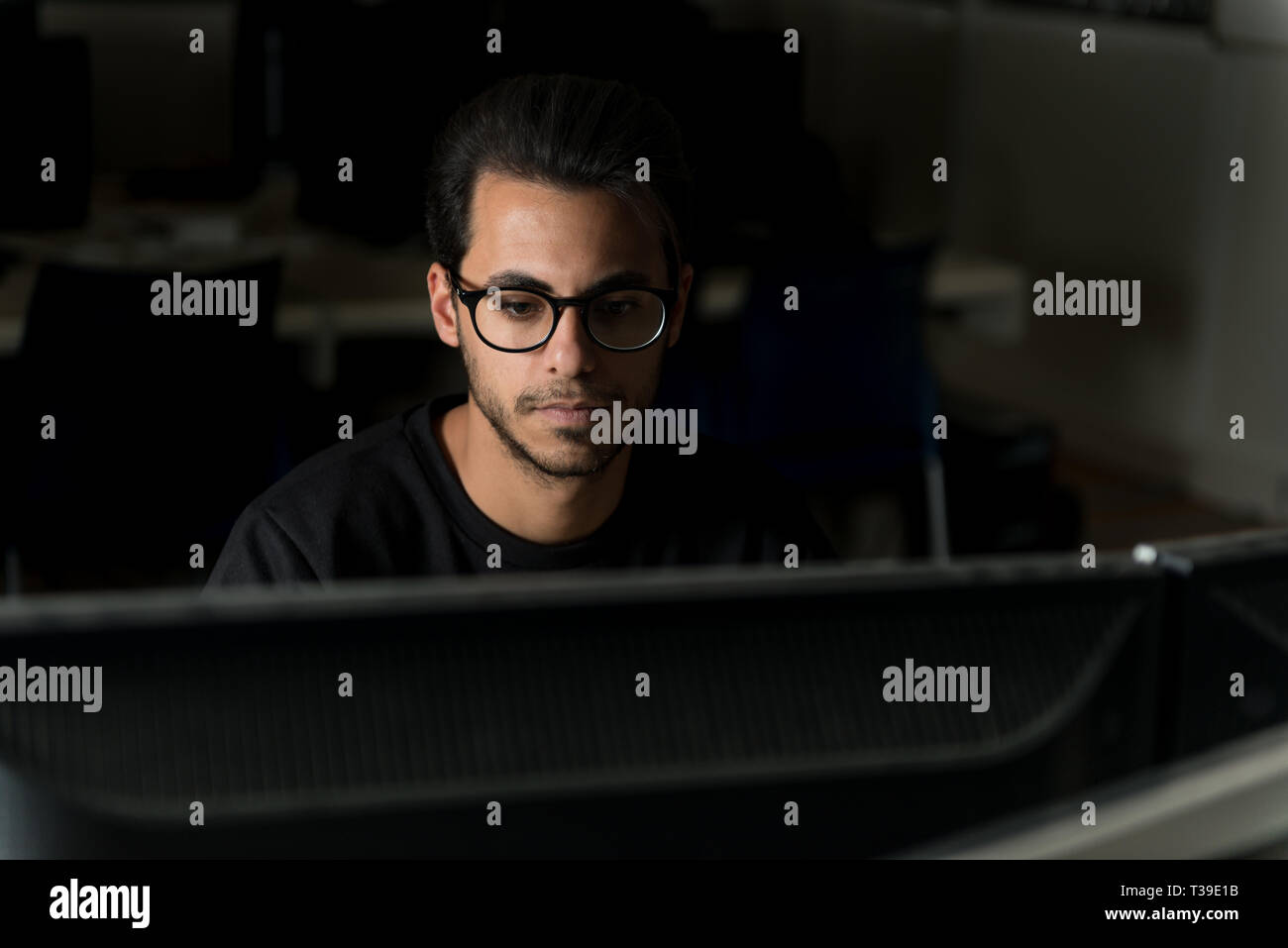 Blick über einen Bildschirm auf dem Gesicht eines jungen Informatik Schüler arbeiten mit dem Computer. Stockfoto