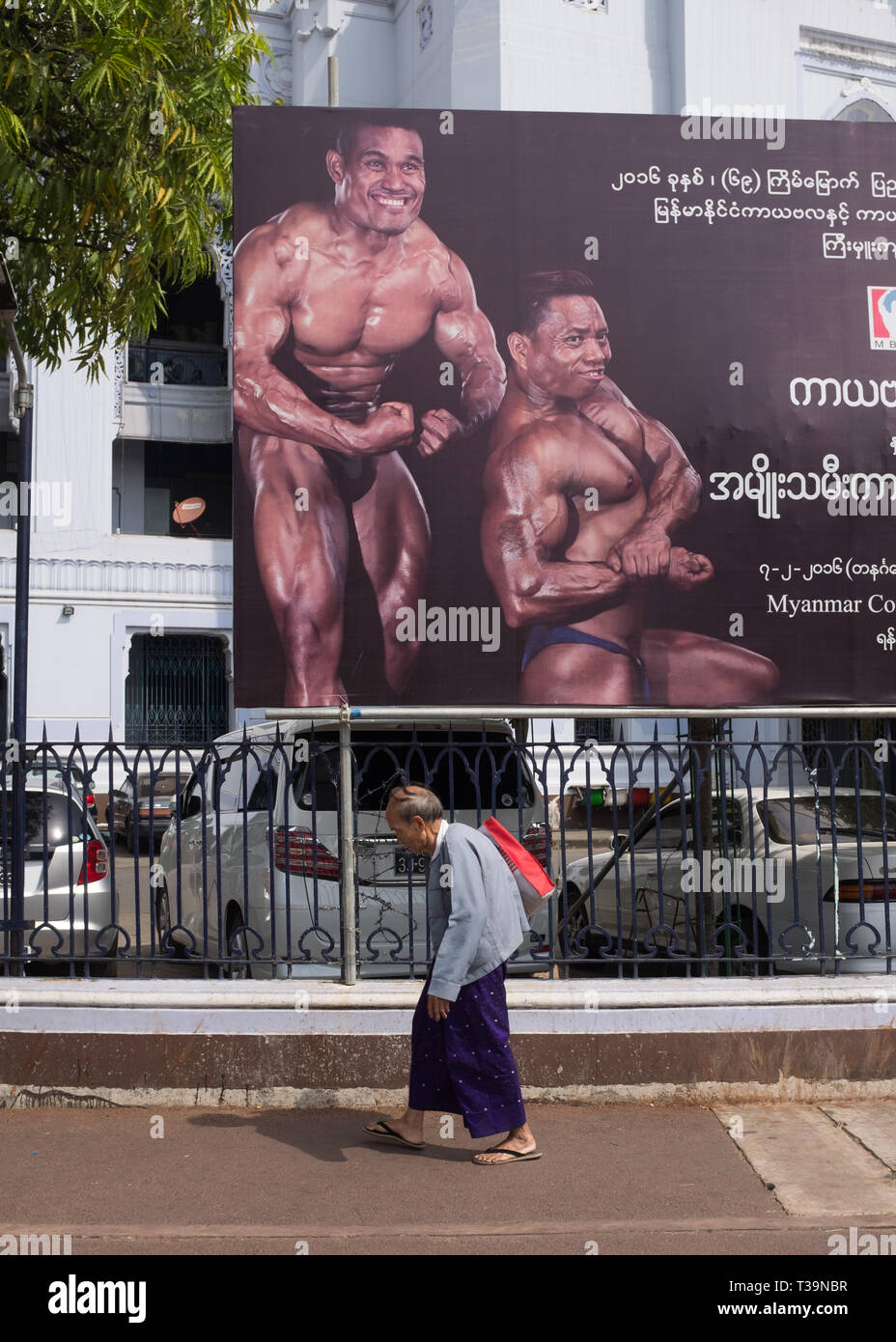 Alter Mann zu Fuß vorbei an einer Plakatwerbung Body Building auf Sule Pagode Kreisverkehr in Yangon (Rangun), Myanmar (Birma) Stockfoto