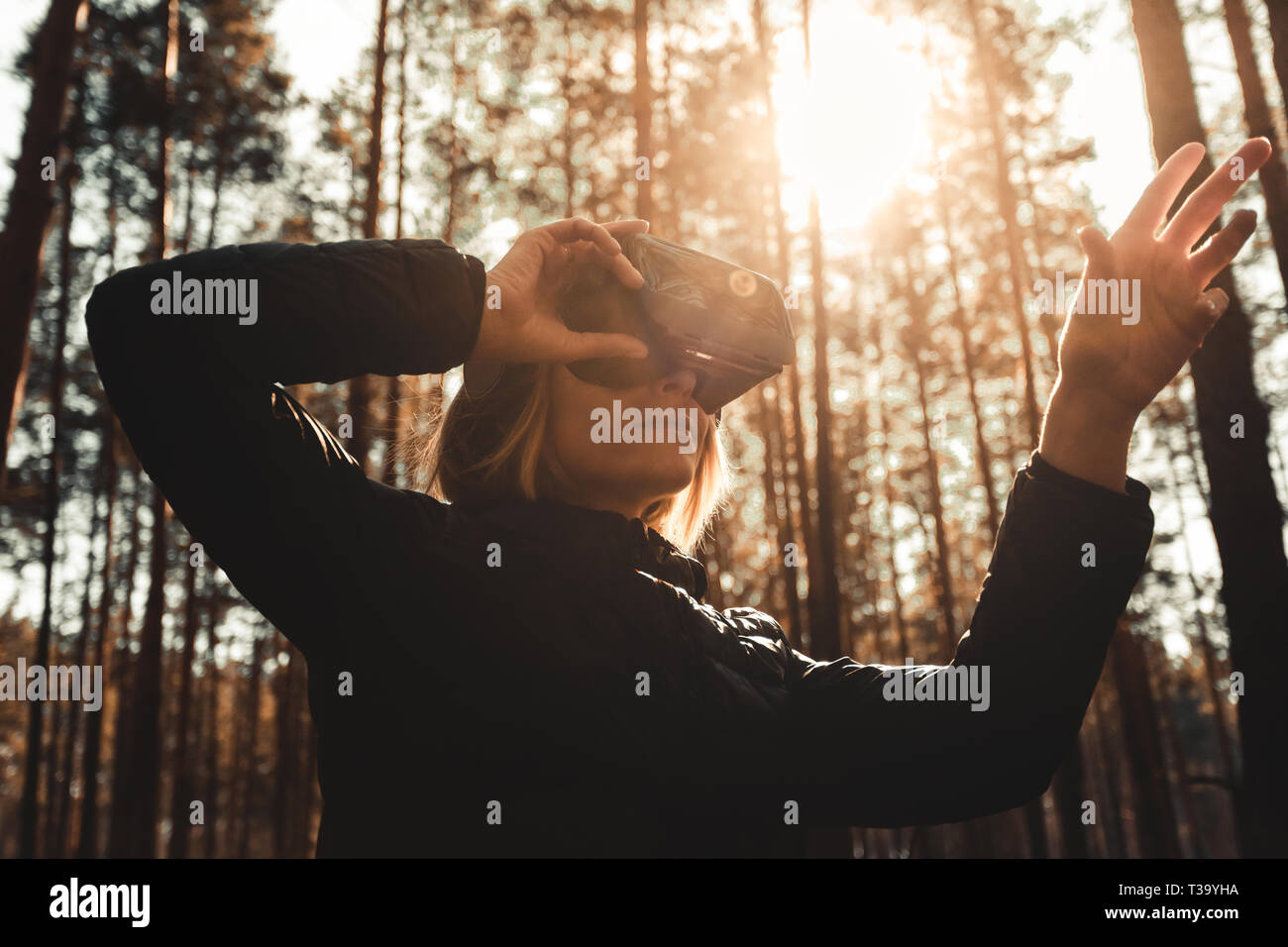 Schöne junge blonde Frau im Wald mit Virtual reality Headset suchen gerade und versucht, etwas mit der Hand zu berühren. VR-Brille, Technolog Stockfoto