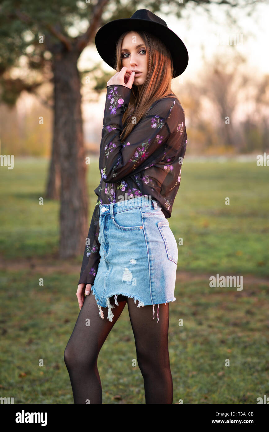 Schöne Brünette in eine durchsichtige schwarze Bluse, zerrissene Jeans rock  und hut. Modische Frau. Casual Wear. Trend Kleidung Stockfotografie - Alamy