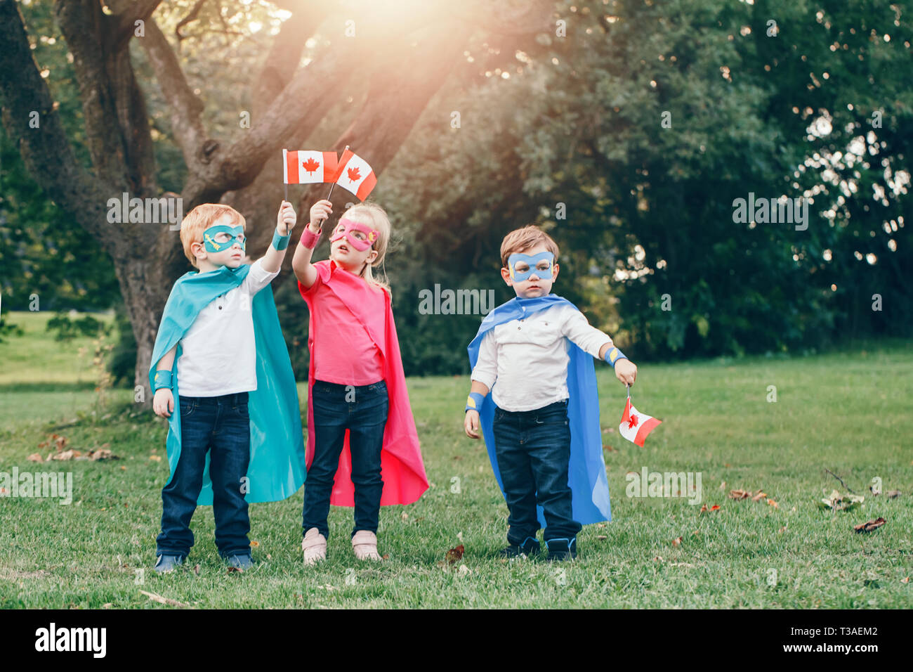 Kaukasische Kinder in Superhelden Kostüme und Masken Holding winken kanadischen Flagge. Jungen, Mädchen feiert Nationalfeiertag Kanada Tag im Sommer, Park Stockfoto