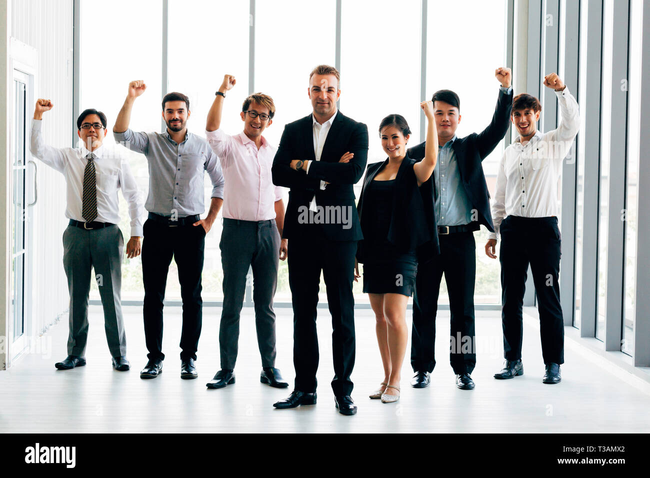 Fröhliche multiethnischen Kollegen Lächeln und die Fäuste, während in der Nähe von zuversichtlich Boss stehen und Erfolge feiern in der Nähe der Fenster im Büro Stockfoto