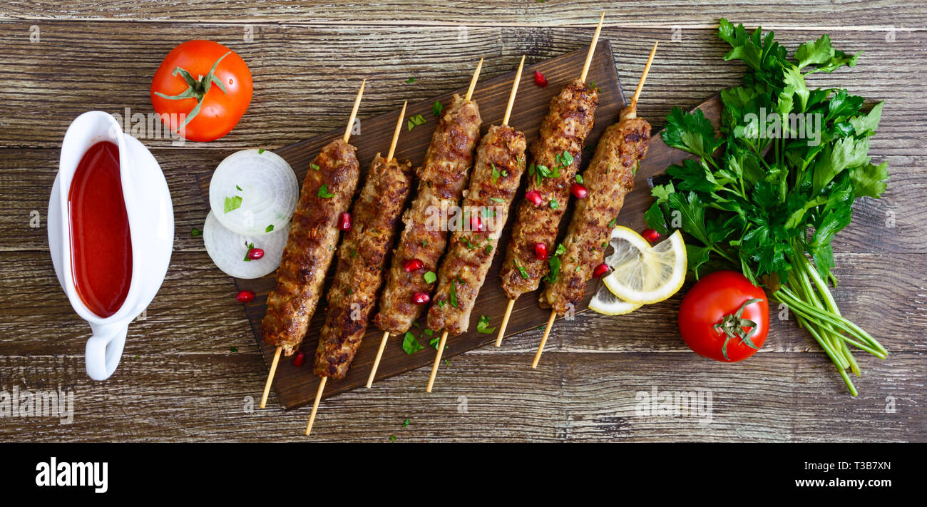 Köstliche lula Kebab auf einem Holztisch. Gehacktes Fleisch auf Holzspieße, gegrillt. Östliche Küche. Ansicht von oben, flach. Banner Stockfoto