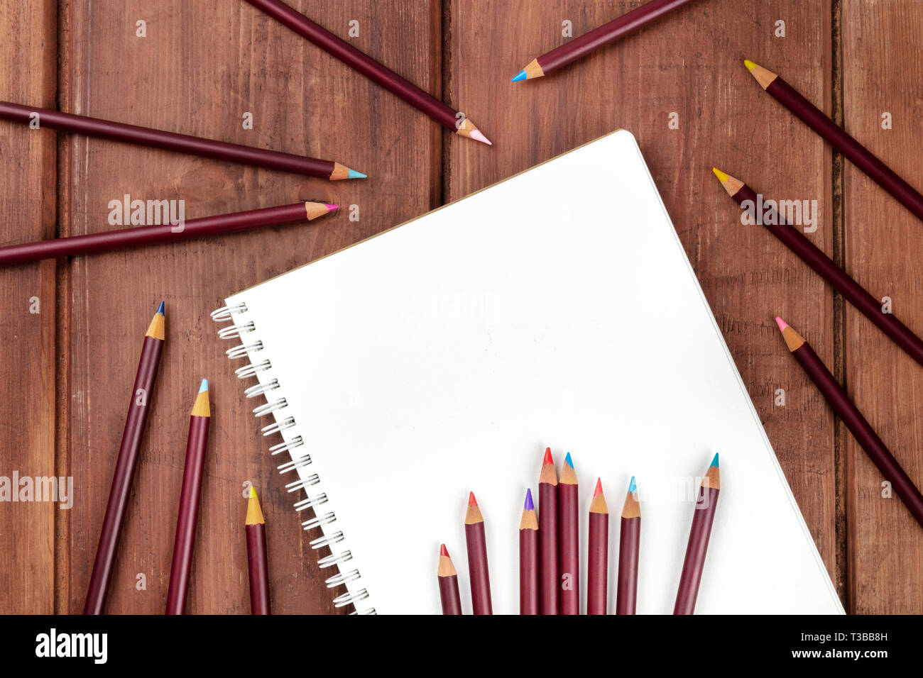 Ein Foto von einem shetchbook mit vielen verschiedenen Farbstifte um ihn herum, geschossen von oben auf einem dunklen Hintergrund mit einem Platz für Text Stockfoto