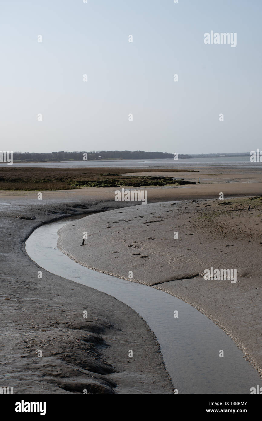 Wicklung Stream Richtung Meer in schlammigen uk Mündung bei Ebbe mit klaren Himmel Stockfoto