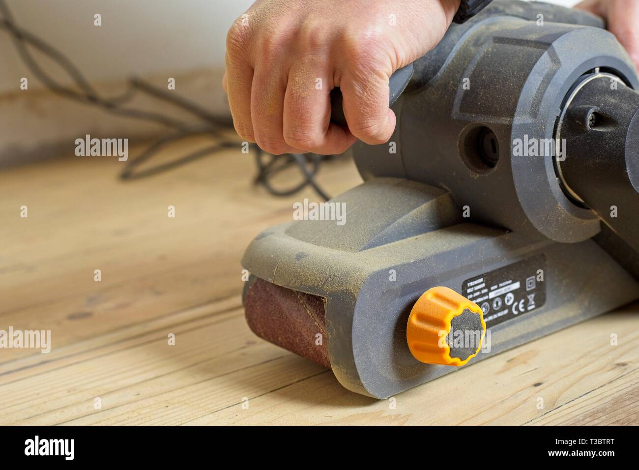 Weibliche mit einem Bandschleifer auf einem mit Pinien Holzboden während DIY und home Renovierungen Stockfoto