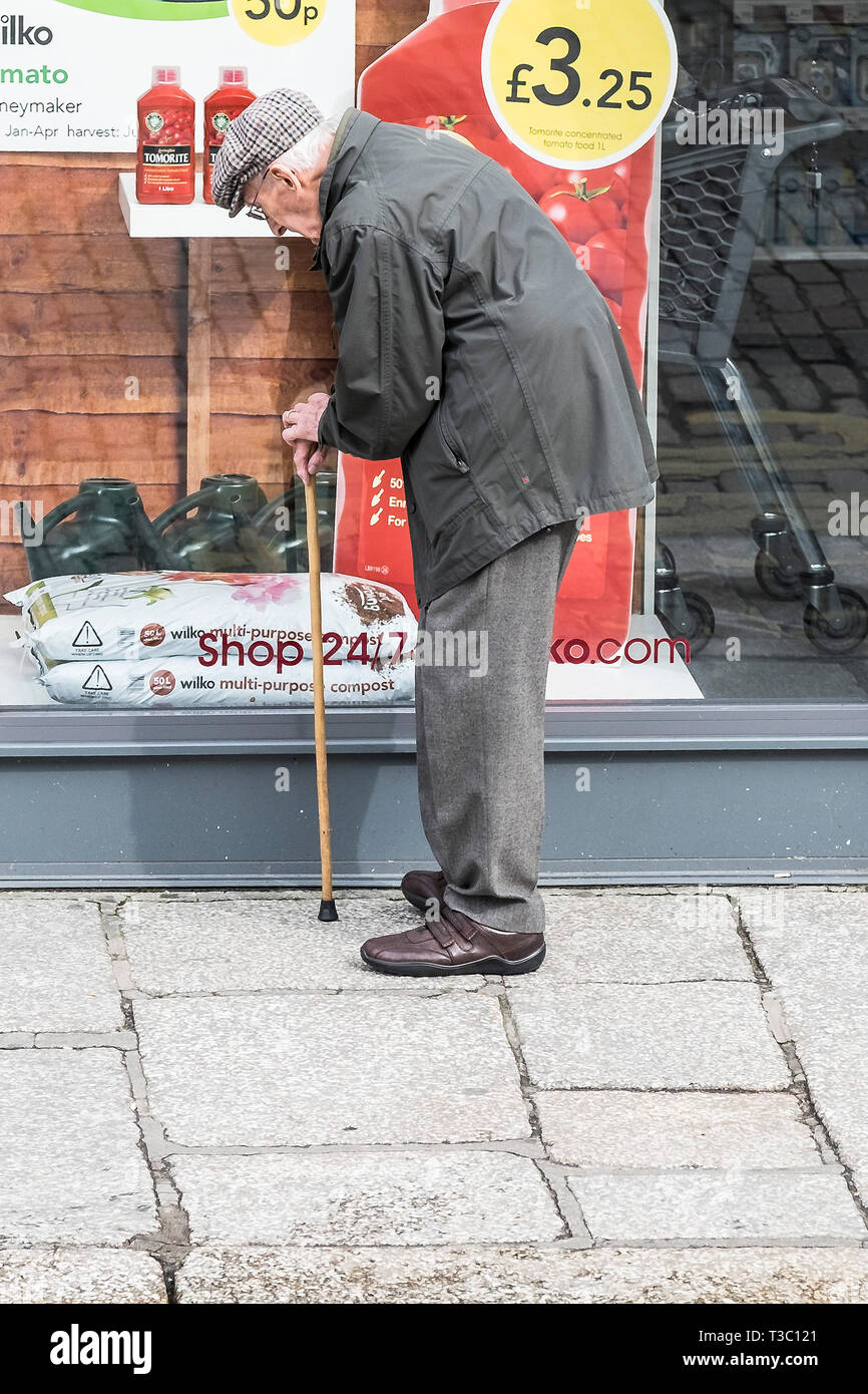 Ein älterer Herr beugte sich über seinen Spazierstock Wie sieht er in einem Schaufenster. Stockfoto