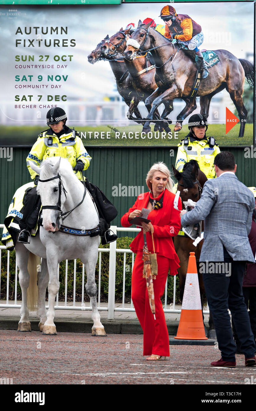 Stilvolle Dame trägt einen roten Hosenanzug steht vor der Polizei Pferde an den 2019 Aintree Grand National Meeting Stockfoto
