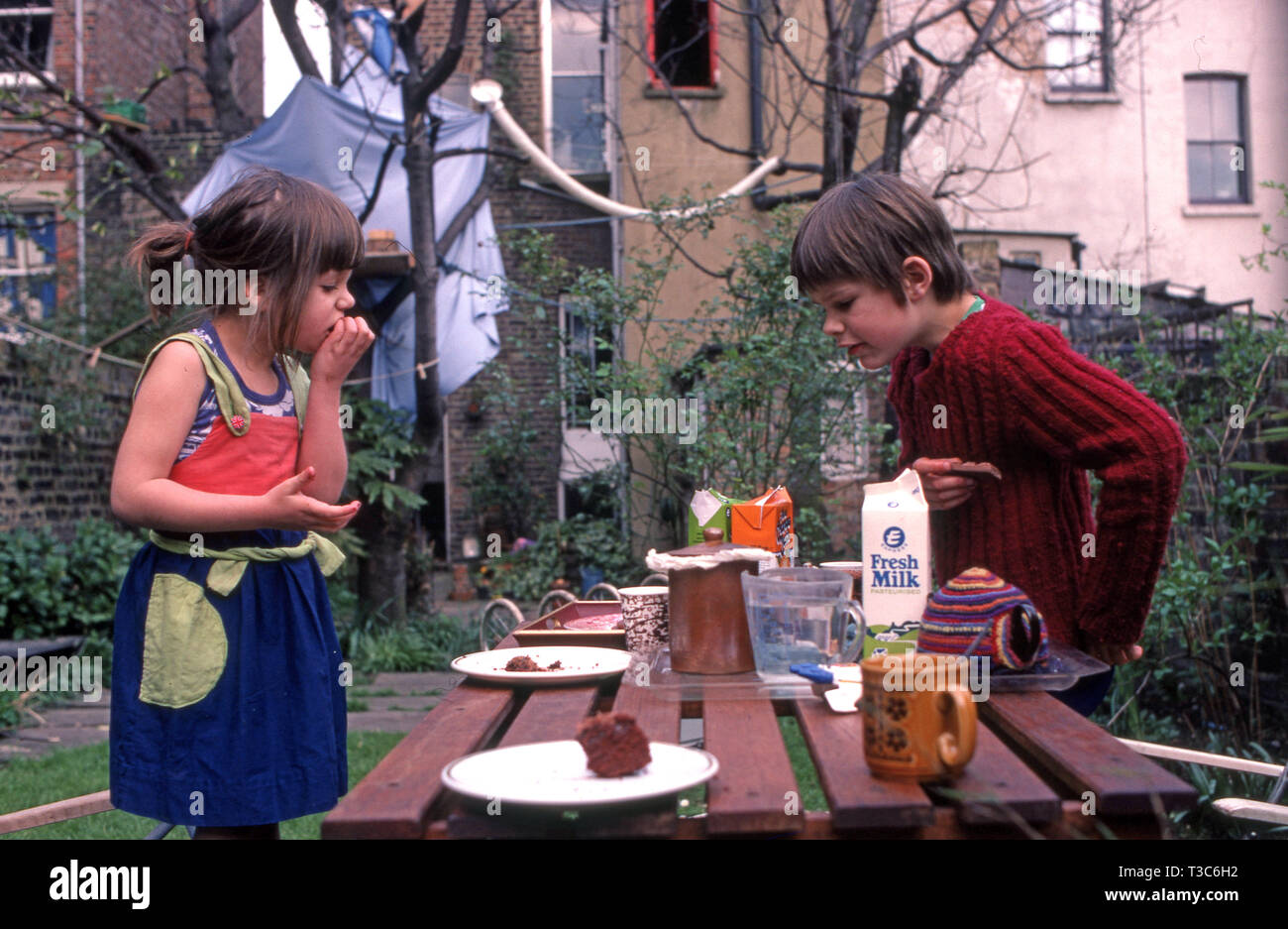 Junge Bruder und Schwester Kuchen essen bei Tisch für Picknick im Garten auf der Rückseite Stockfoto