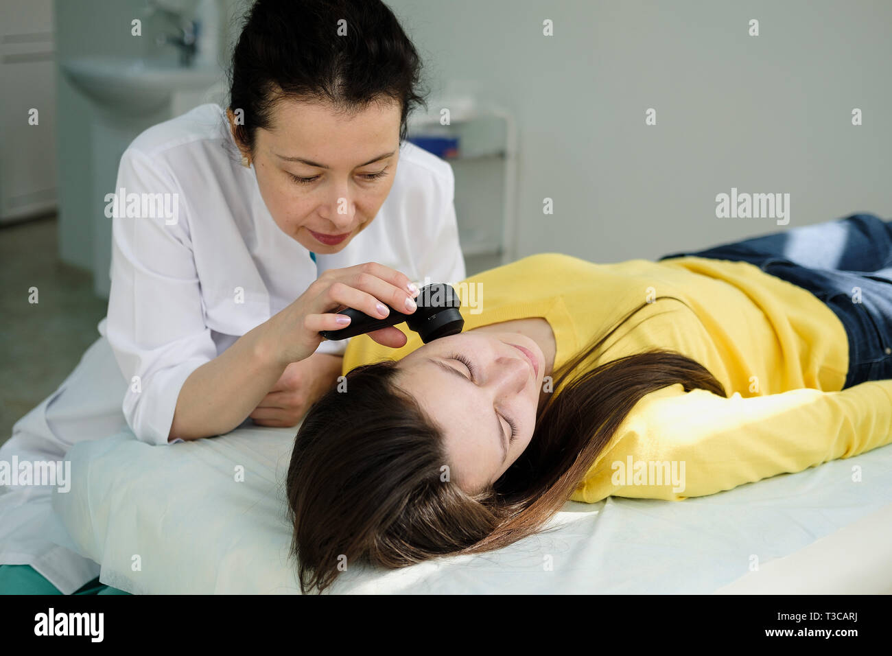 Weibliche Dermatologe mit einem professionellen Dermatoskop beim Tun der Haut Untersuchung, Kontrolle gutartige Muttermale im Gesicht. Dermatologe Muttermal untersuchen Stockfoto