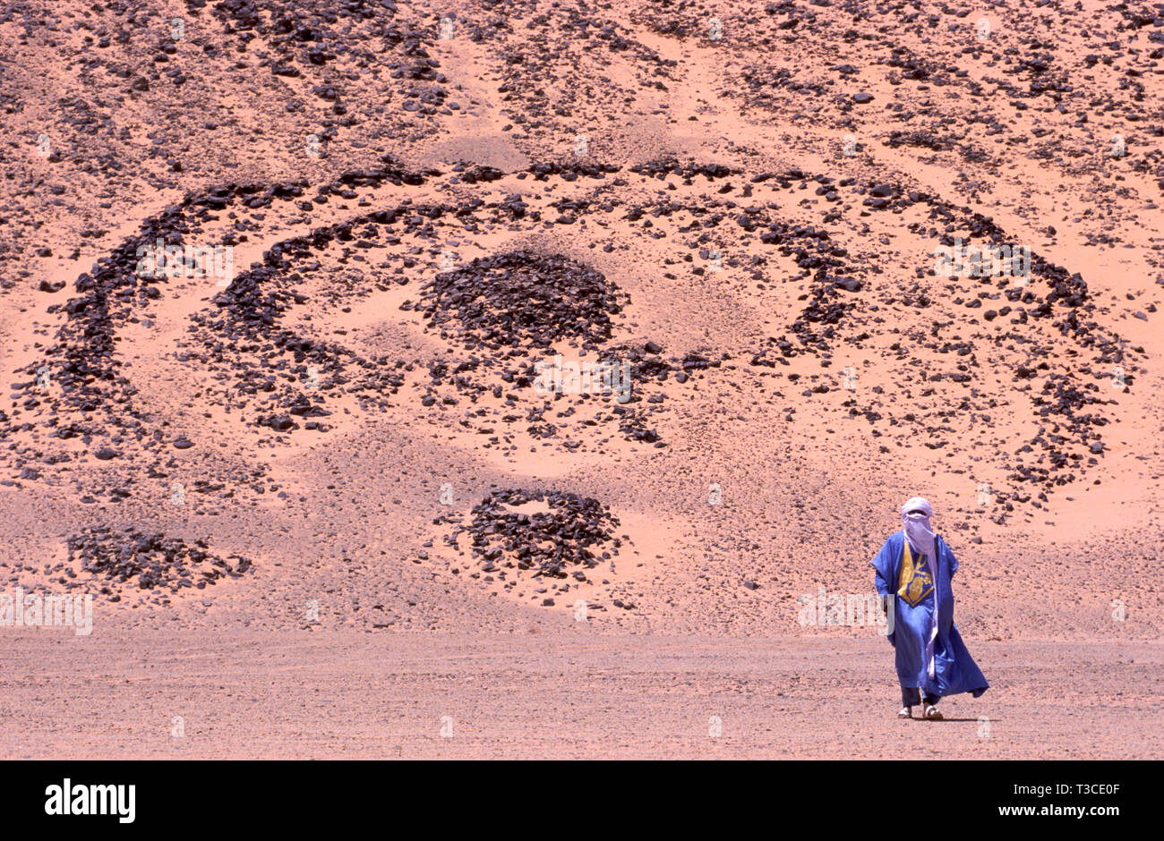 Tuareg Mann in einer Tracht mit einem 5000 Jahre alten Grab im Hintergrund in der Sahara in Algerien Stockfoto