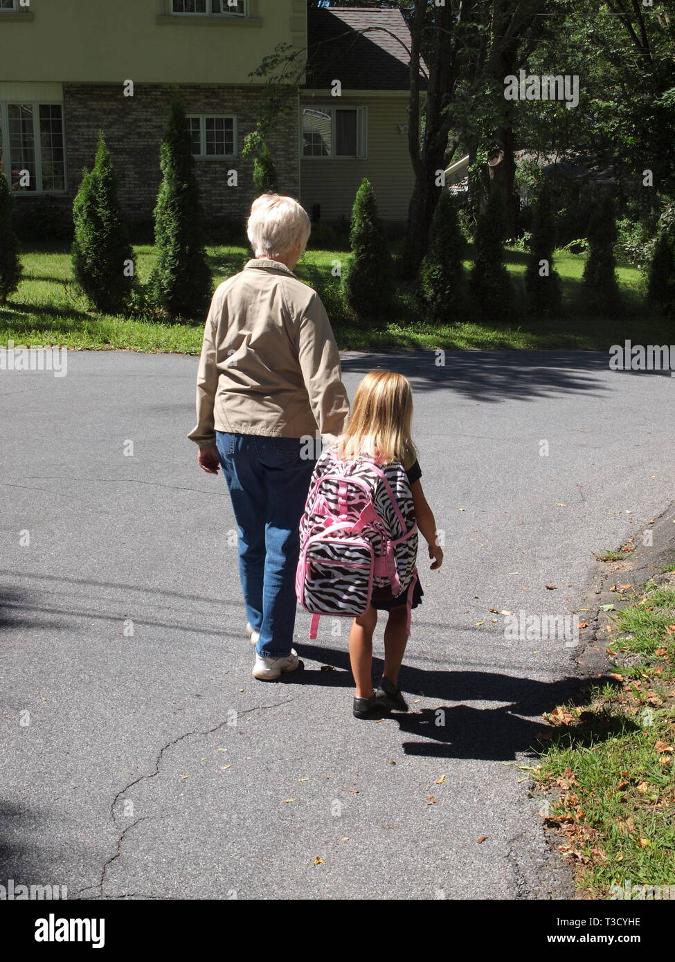 Kleine Mädchen zu Fuß zu ihrer Schule Bus am ersten Tag der Schule. Halten sie ihre Großmütter die Hand mit einem großen, rosa gestreifte Back Pack. Stockfoto