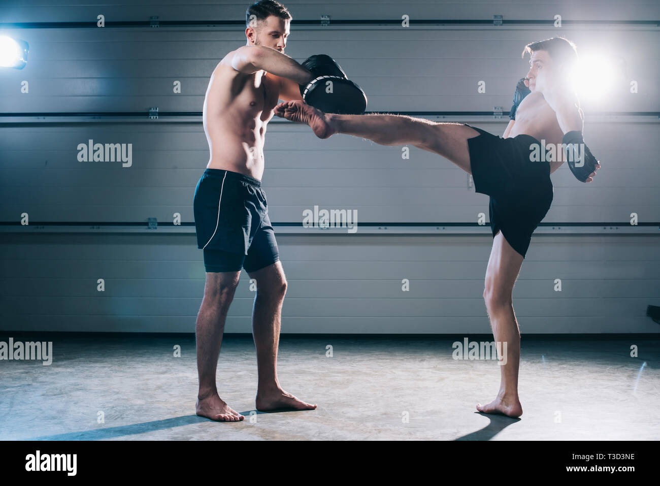 Starke muskuläre shirtless MMA-Kämpfer üben High Kick mit einem anderen Sportler während des Trainings Stockfoto
