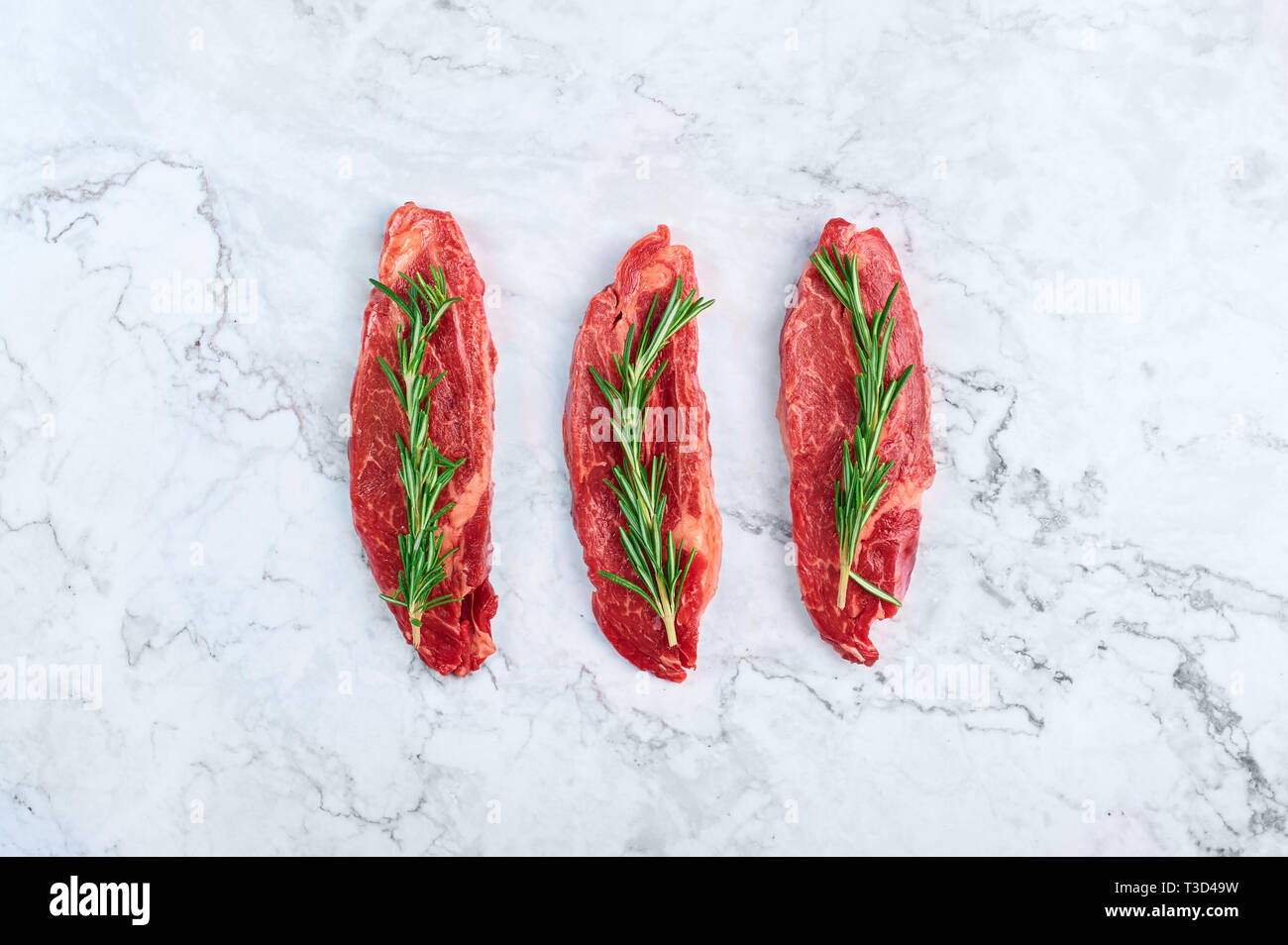Raw marmoriert Rindersteaks mit grünen Zweig Rosmarin in weißem Marmor Hintergrund. Kopieren Sie Platz Stockfoto