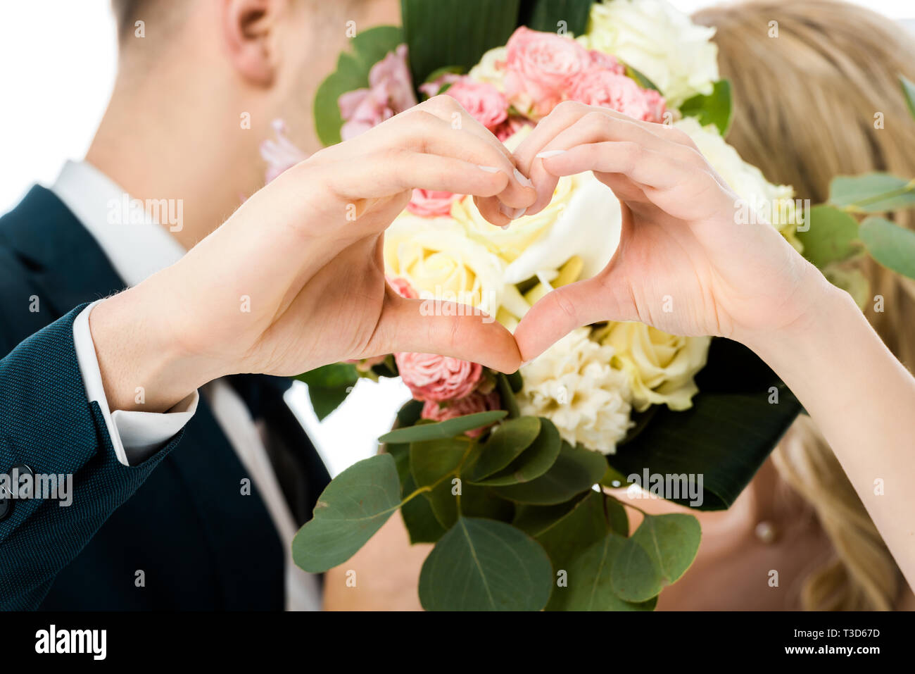 Selektiver Fokus von Bräutigam und Braut zeigen Herz zeichen mit den händen, beim Verstecken Gesichter hinter wedding bouquet isoliert auf weißem Stockfoto