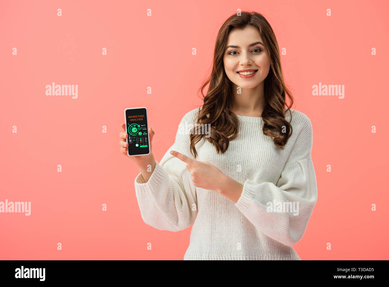 Frau in weißem Pullover zeigt mit dem Finger auf Smartphone mit Charts auf dem Bildschirm isoliert auf Rosa Stockfoto