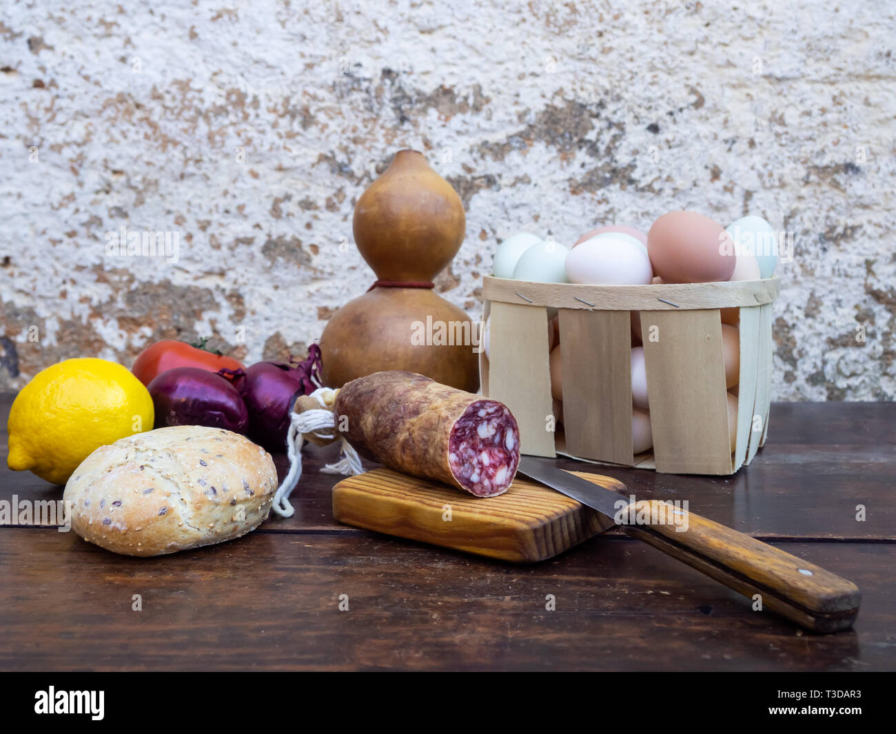 Traditionelle spanische Küche auf einem alten Holztisch, iberischen Schwein Wurst, Brot, Eier, Käse und Gemüse und ein altes Messer Stockfoto