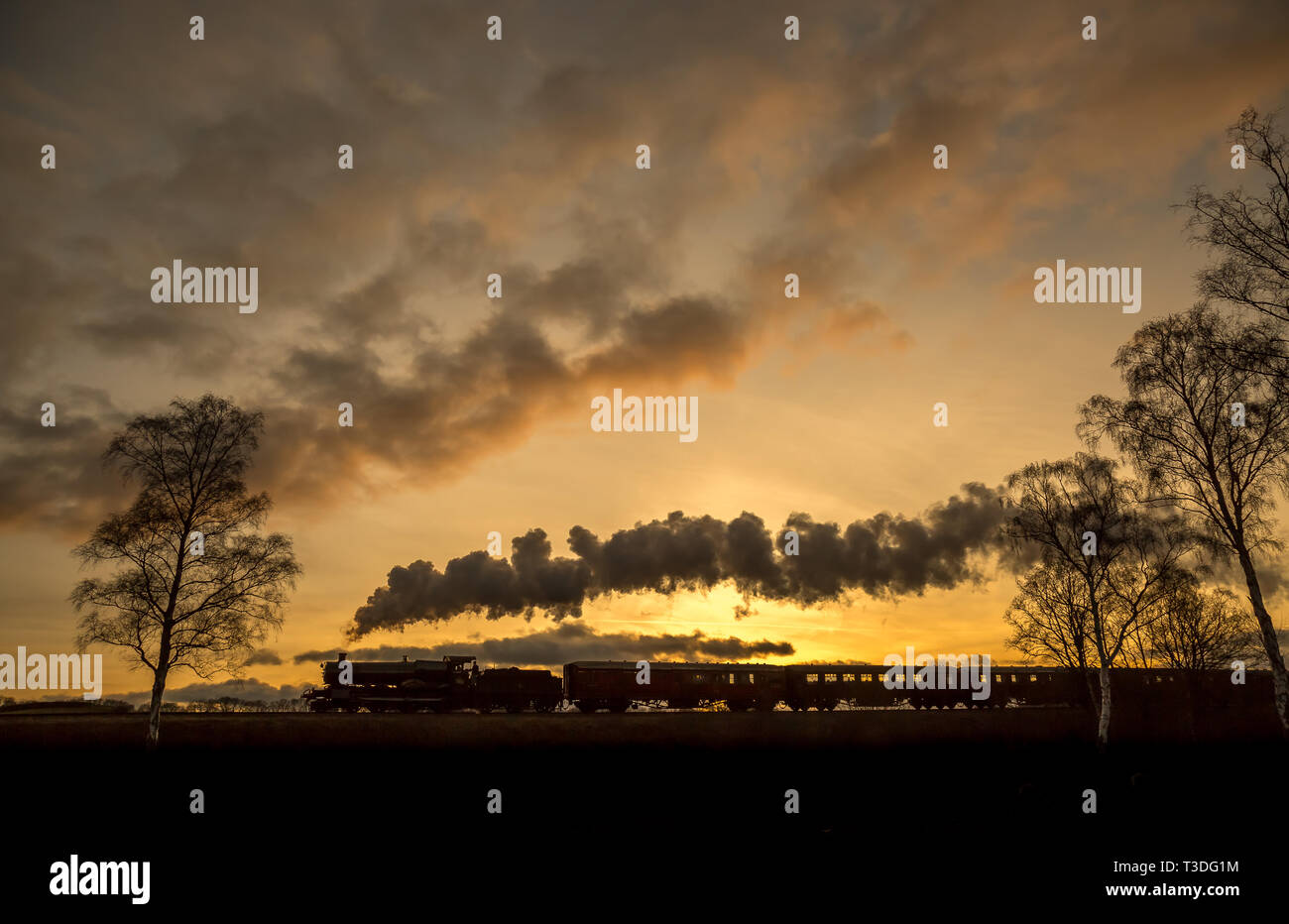 Dramatische malerische Seitenansicht der bewegten Vintage UK Dampfzug Silhouette in Sonnenuntergang, vorbei an Landschaft, die Dampf, Rauch puffend. Stockfoto