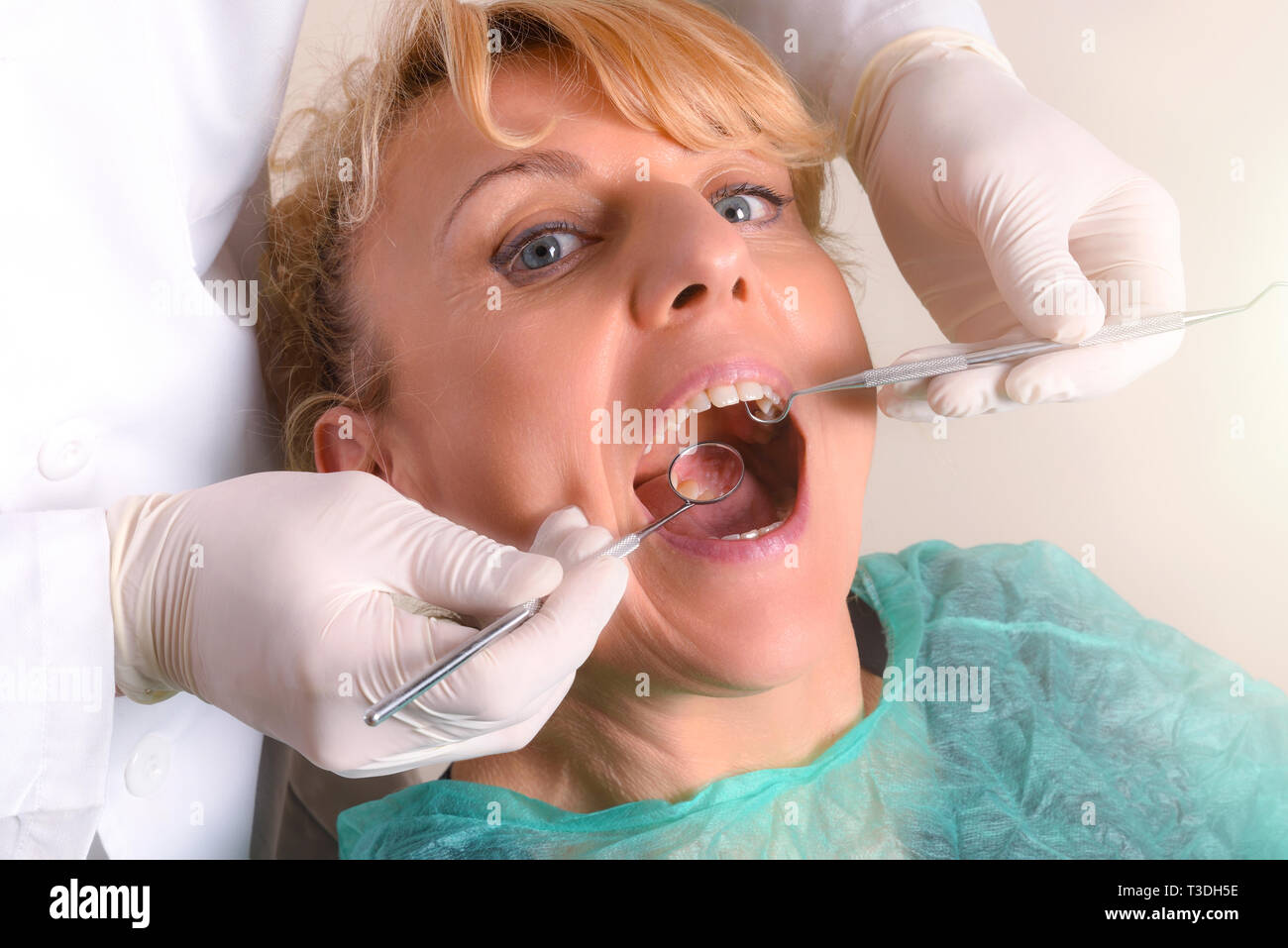 Zahnarzt mit weissem Latex Handschuhe Kontrolle der Mund einer blonden Frau im grünen Kleid mit Gaze isoliert Hintergrund. Horizontale Komposition. Erhöhte vi. Stockfoto