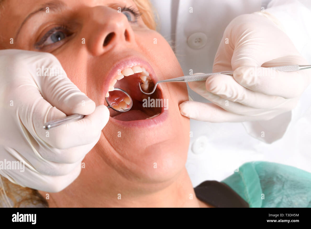 Zahnarzt mit weissem Latex Handschuhe Prüfung der Mund der blonde Frau in Grün gaze Kleid mit isolierten Hintergrund. Horizontale Komposition. Erhöhte v Stockfoto