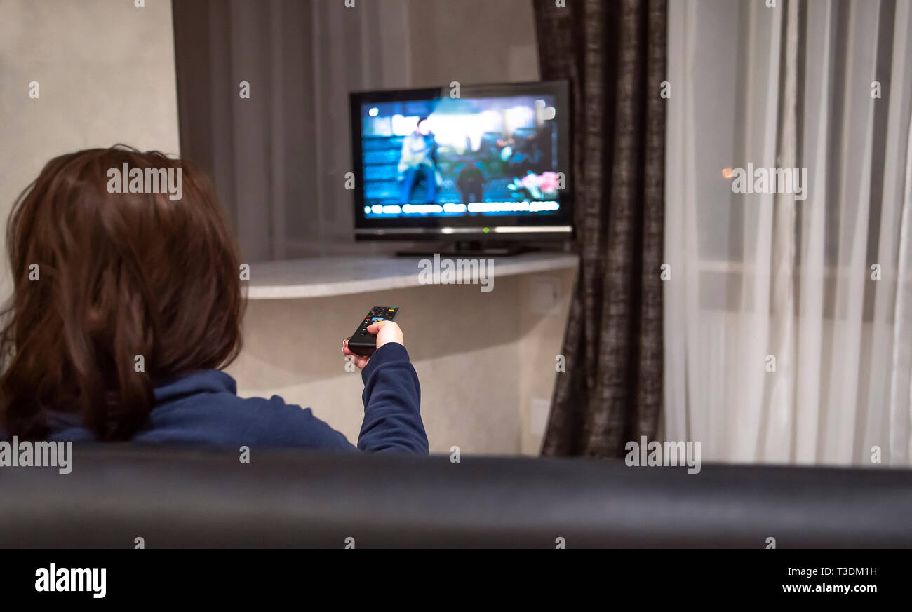 Frau schaltet TV-Kanäle während der Sitzung zu Hause auf der Couch, Rückansicht Stockfoto