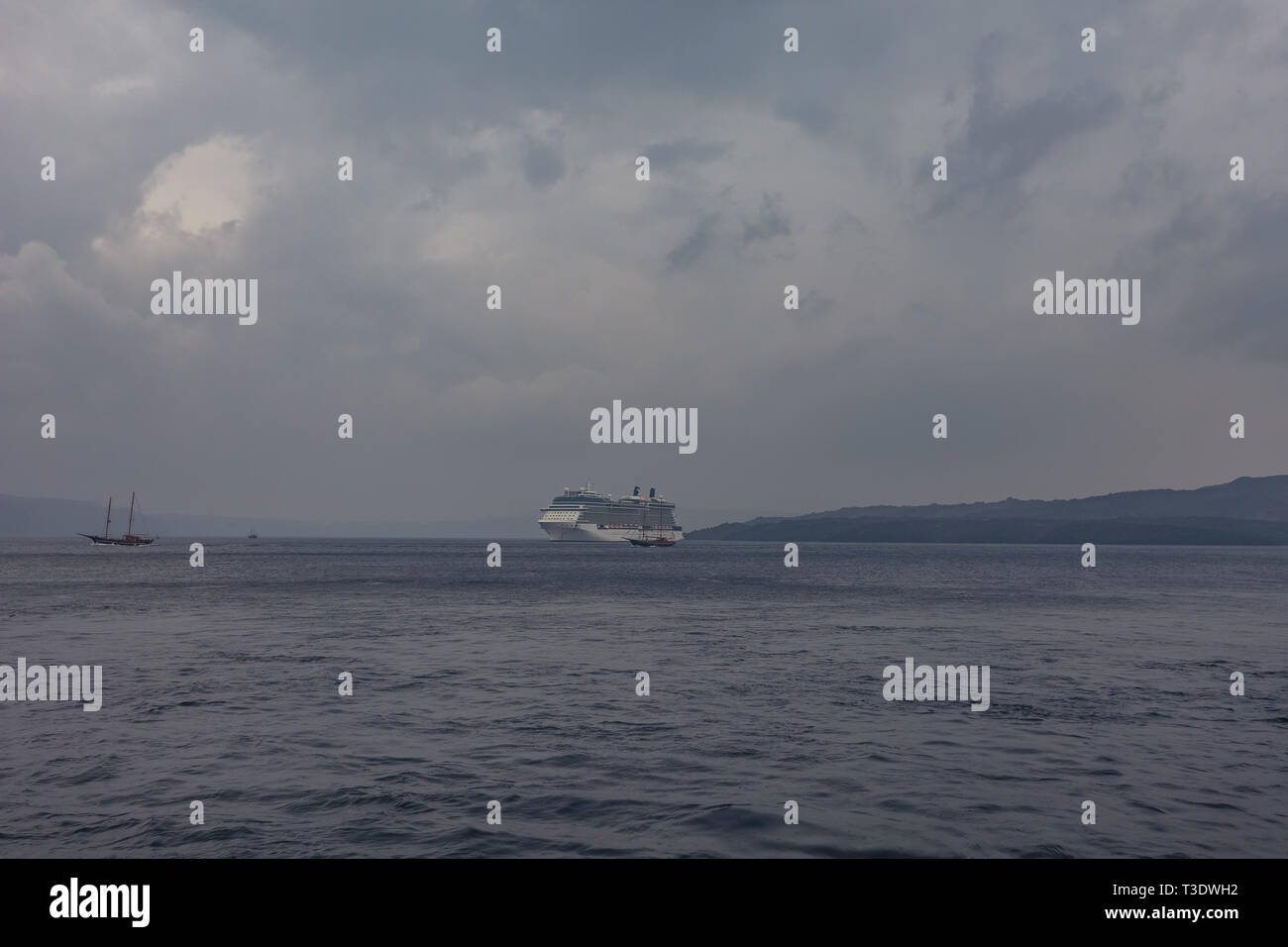 Panorama von Santorini an einem bewölkten Tag, mit Kreuzfahrtschiff Warten im Hafen, Kykladen, Griechenland Stockfoto