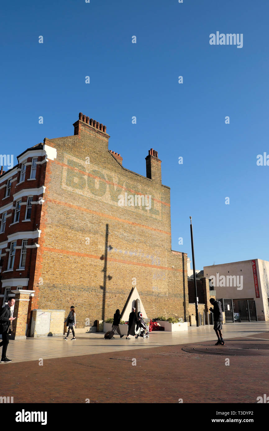 Vertikale Ansicht von Menschen zu Fuß Fußgänger in Windrush Square und dem bovril Gebäude mit blauen Himmel in Brixton South London England UK KATHY DEWITT Stockfoto