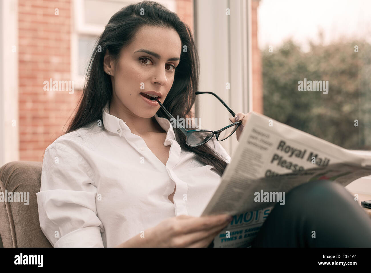 Schwarzhaarige Frau liest eine Zeitung an Kamera suchen Stockfoto