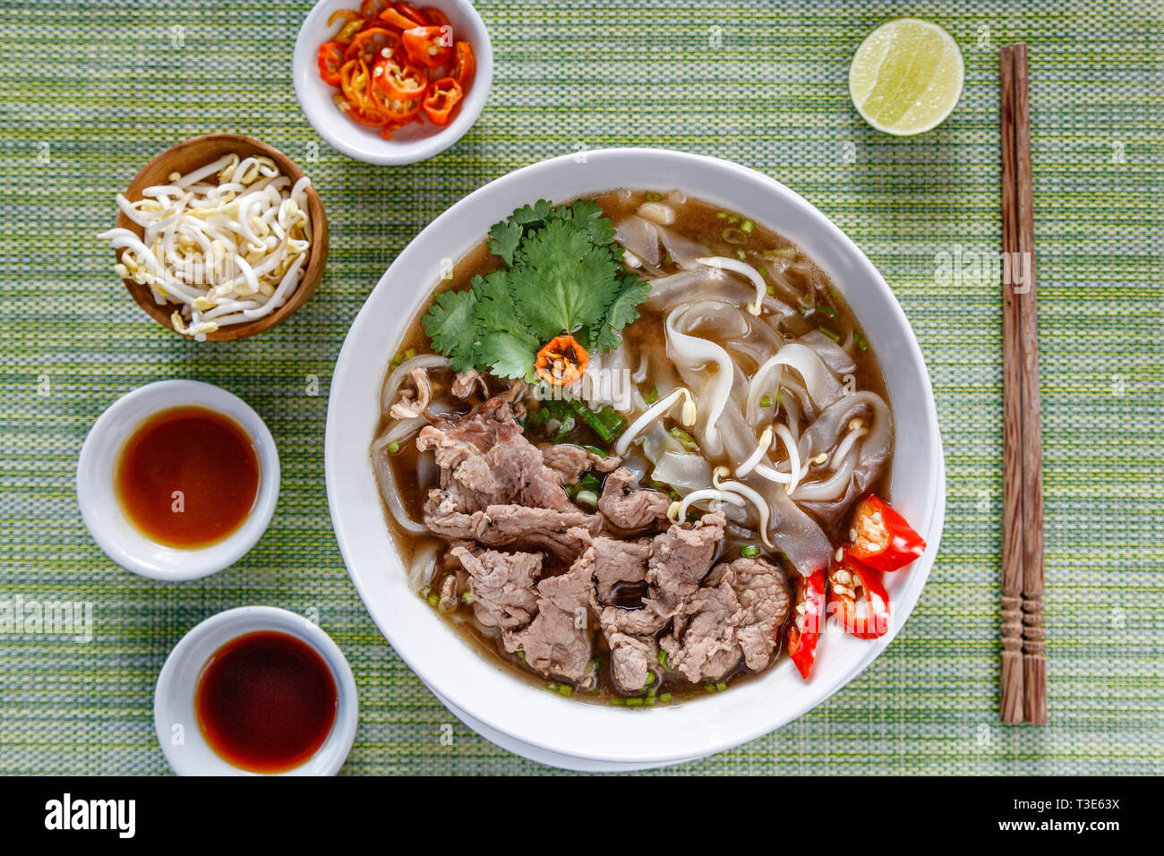 Vietnamesischen traditionellen Rindfleisch und Nudelsuppe Pho Bo in Weiße, runde Schüssel serviert, mit Saucen, Kalk, Chili und Sojasprossen. Holz- Stäbchen. Stockfoto
