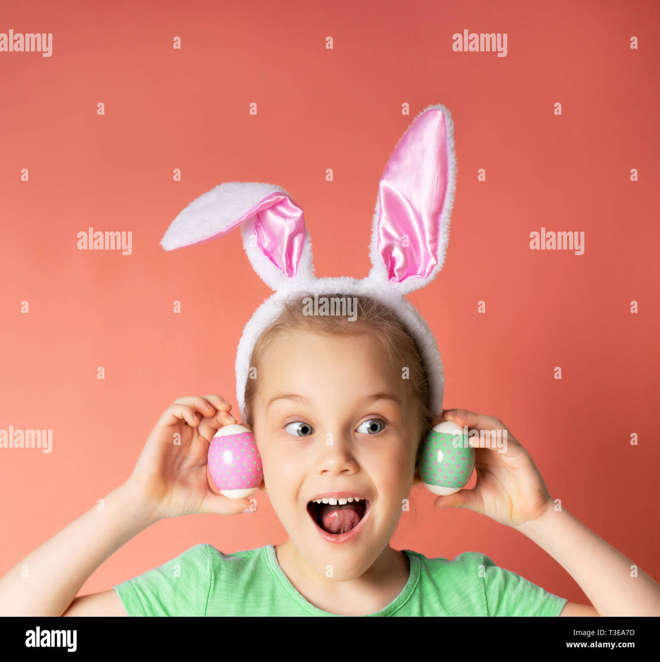 Ostern weibliches Kind Portrait. Nett überrascht Kleines Mädchen mit Hasenohren auf einem rosa Hintergrund hält zwei bunte Polka Dots Eier. lustige Emotionen, lassen Sie sich überraschen. Copyspace für Text. Stockfoto