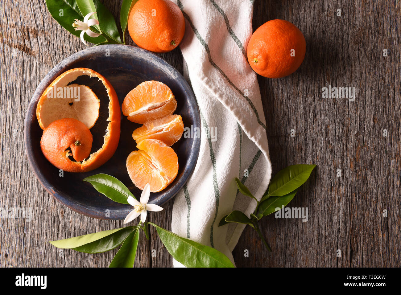 Minneola Tangelo: Nahaufnahme von geschälten Früchte auf einem Teller mit Handtuch und Blätter auf einem rustikalen Holztisch. Stockfoto