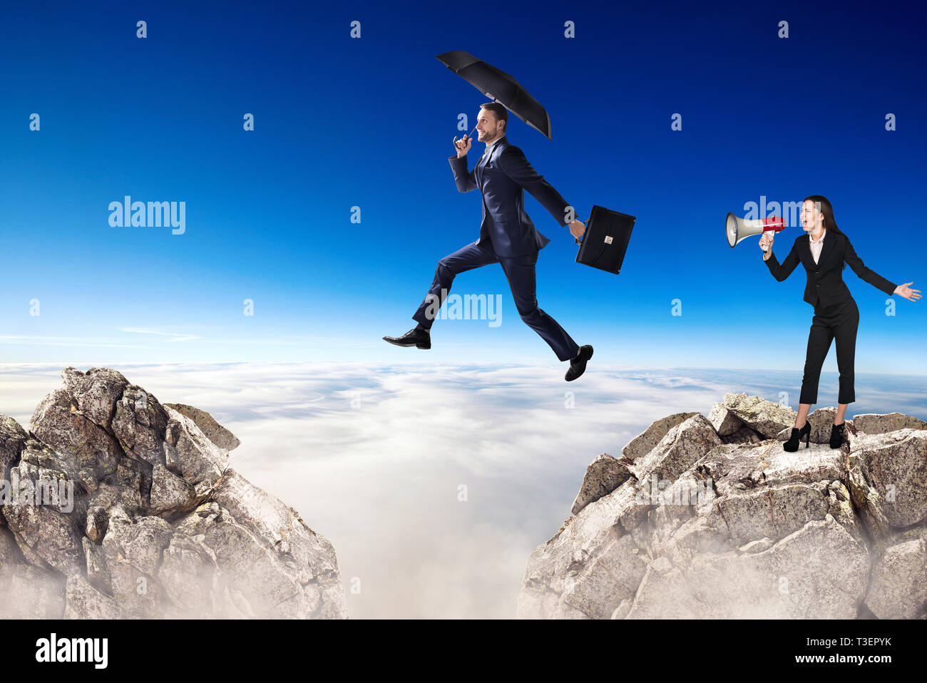 Geschäftsmann springt über eine Klippe und Kollege jubelt mit Megaphon. Stockfoto