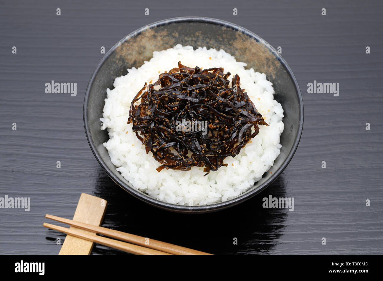 Japanisches Essen, Tsukudani der konbu auf gekochten Reis weiß auf schwarzem Hintergrund Stockfoto