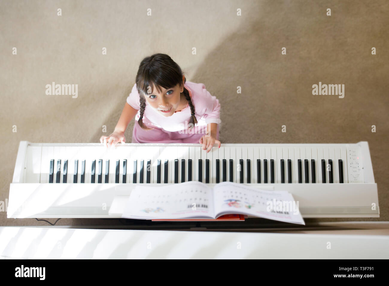 6-7 Jahre altes Mädchen ist Klavier spielen und schauen in die Kamera. Stockfoto