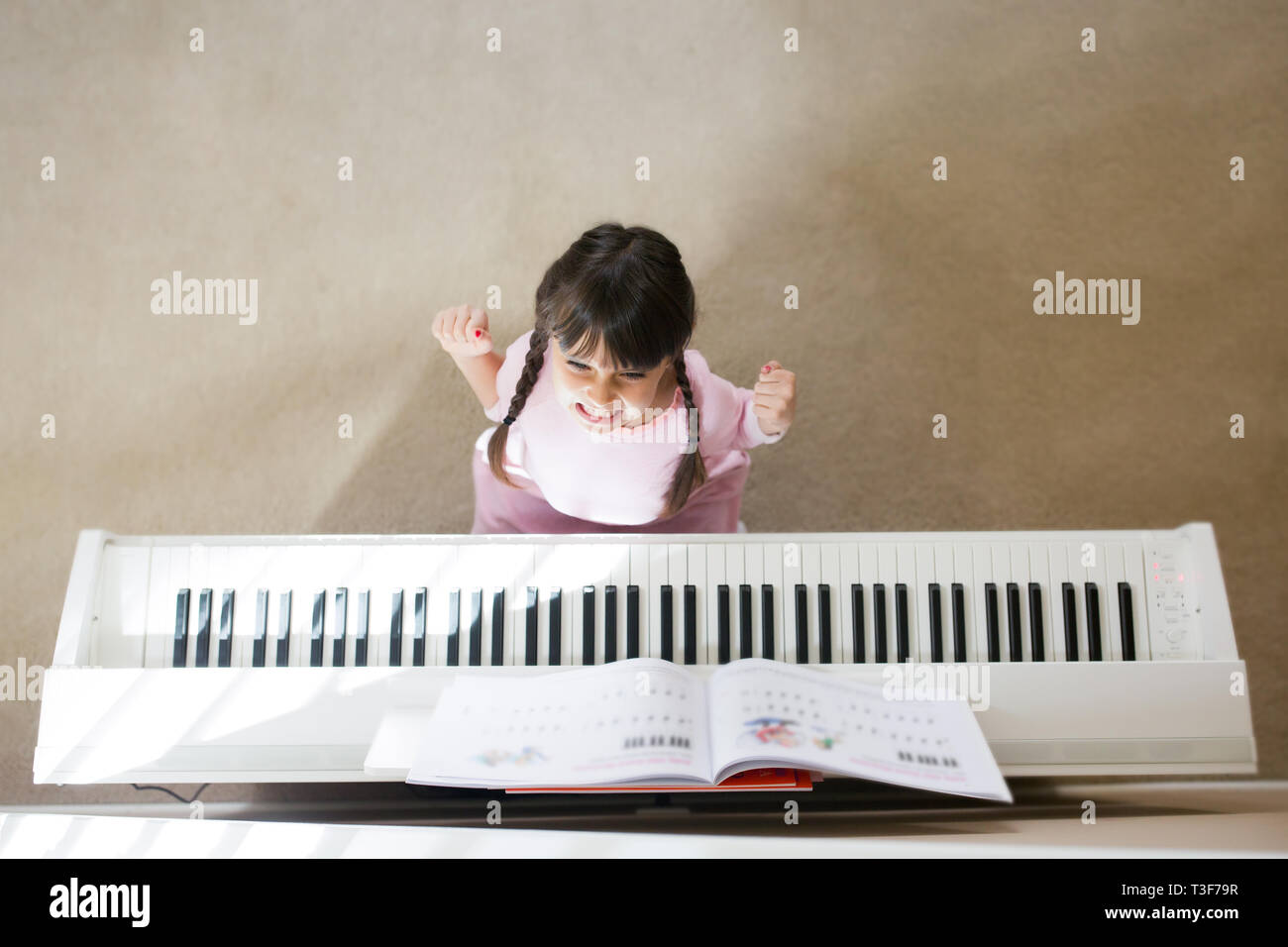6-7 Jahre alt ist nicht glücklich, Klavier zu spielen. Sie hat einen wütenden Gesichtsausdruck. Stockfoto