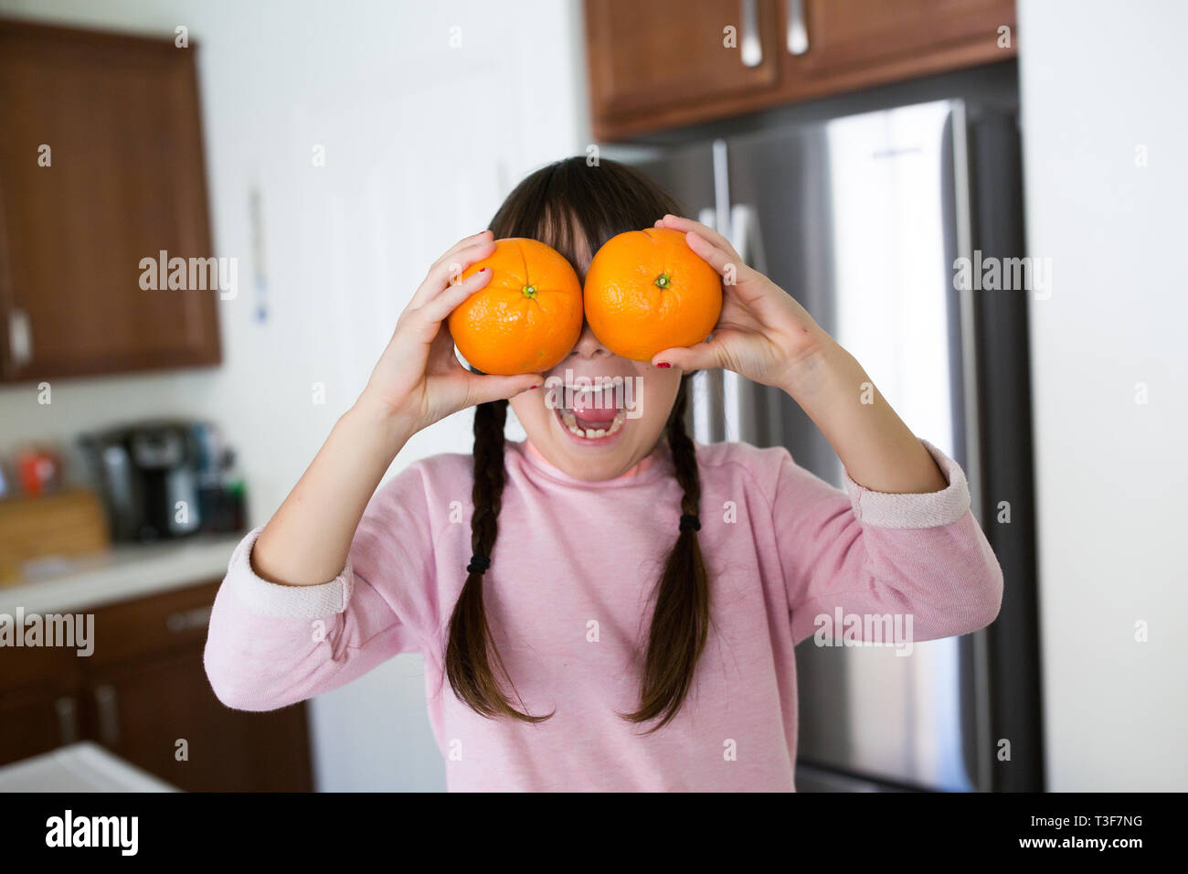 6-7 Jahre altes Mädchen hält Orangen in die Augen. Sie hat eine toothy Lächeln. Stockfoto