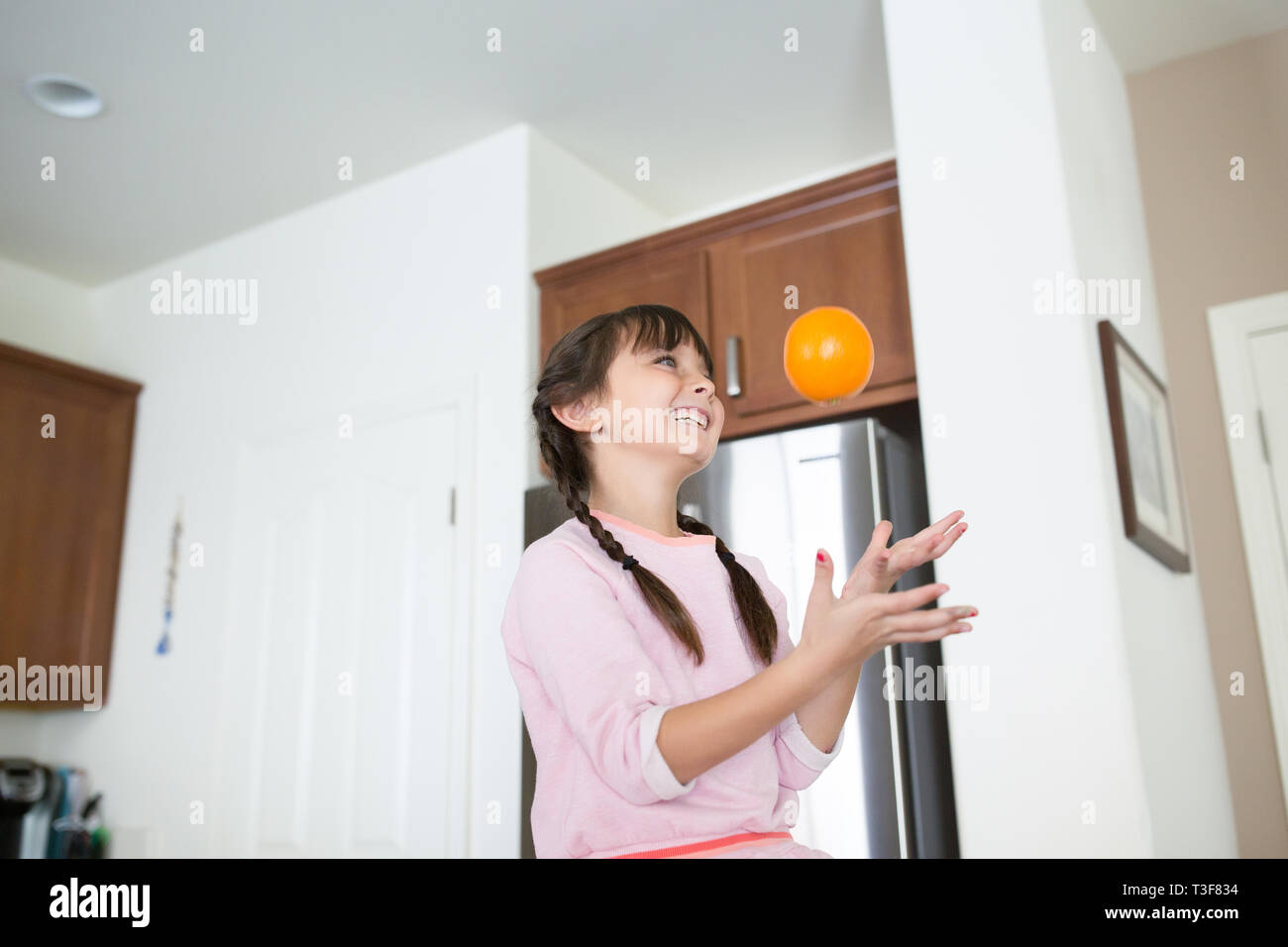 6-7 Jahre altes Mädchen spielt mit Orangen in der Küche. Stockfoto